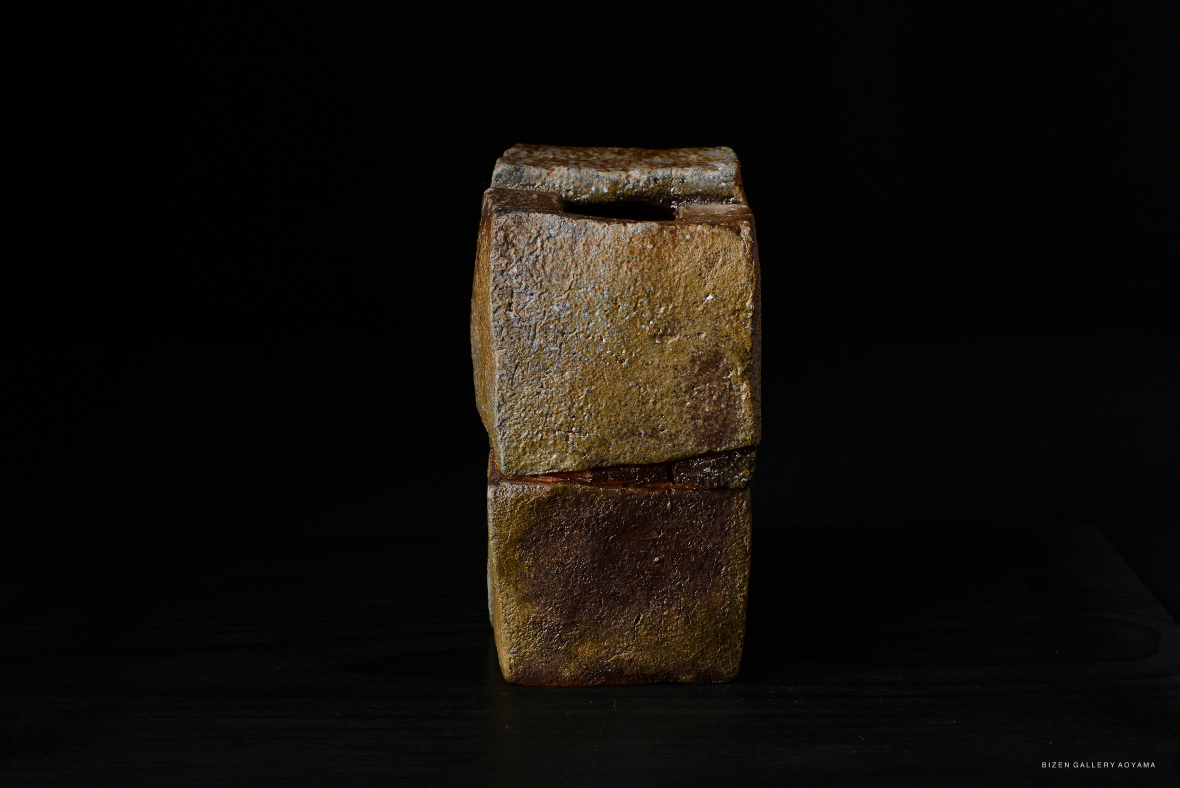 A unique piece of ceramic art, featuring a textured, rectangular form in earthy tones, set against a dark background.