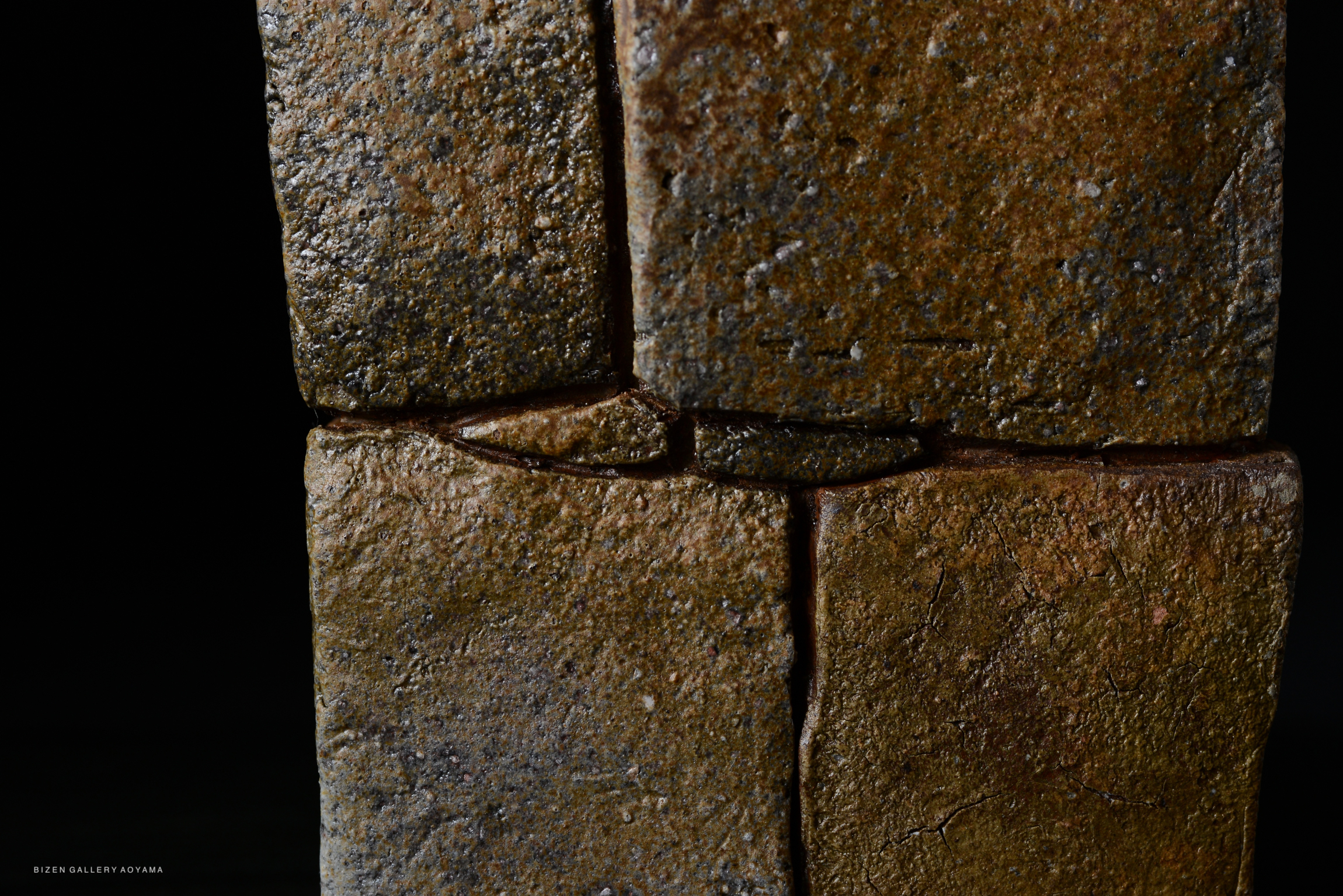 Close-up of textured, earthy ceramic tiles with subtle cracks and variations in color, displayed against a dark background.