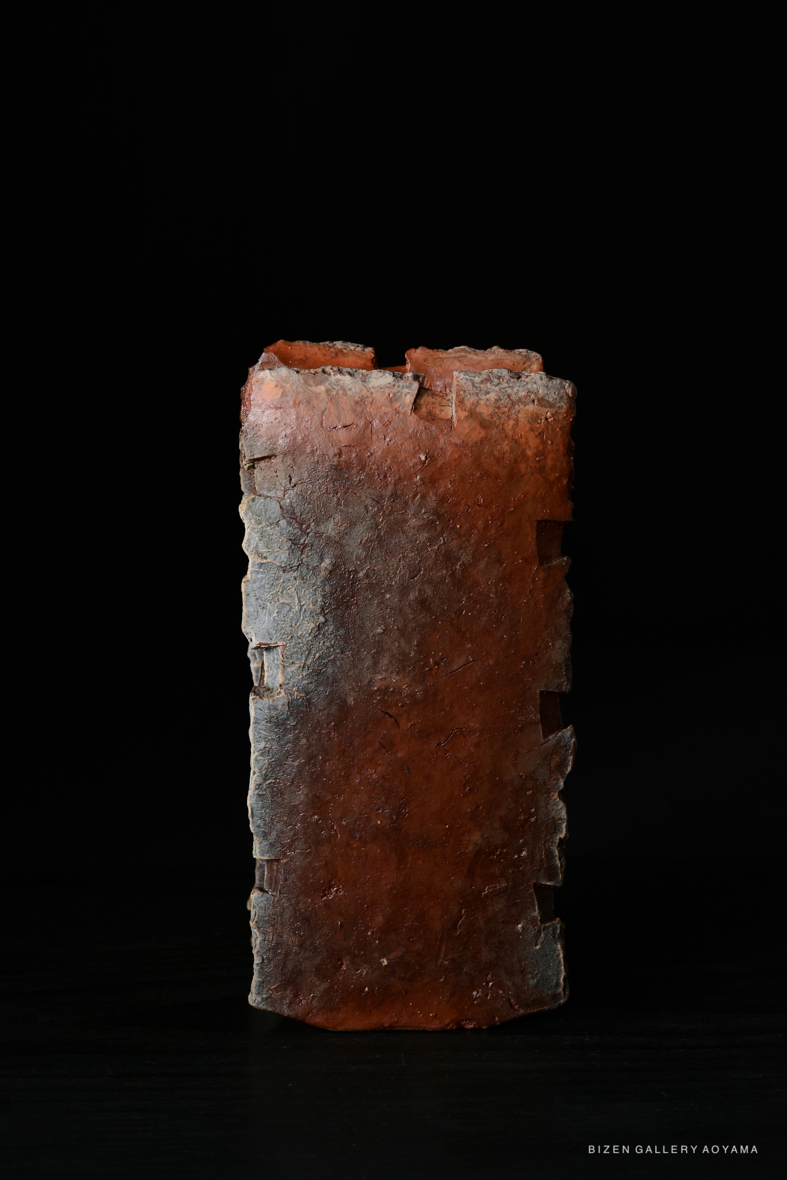 A rectangular ceramic piece with a rough texture and a reddish-brown color, set against a black background.