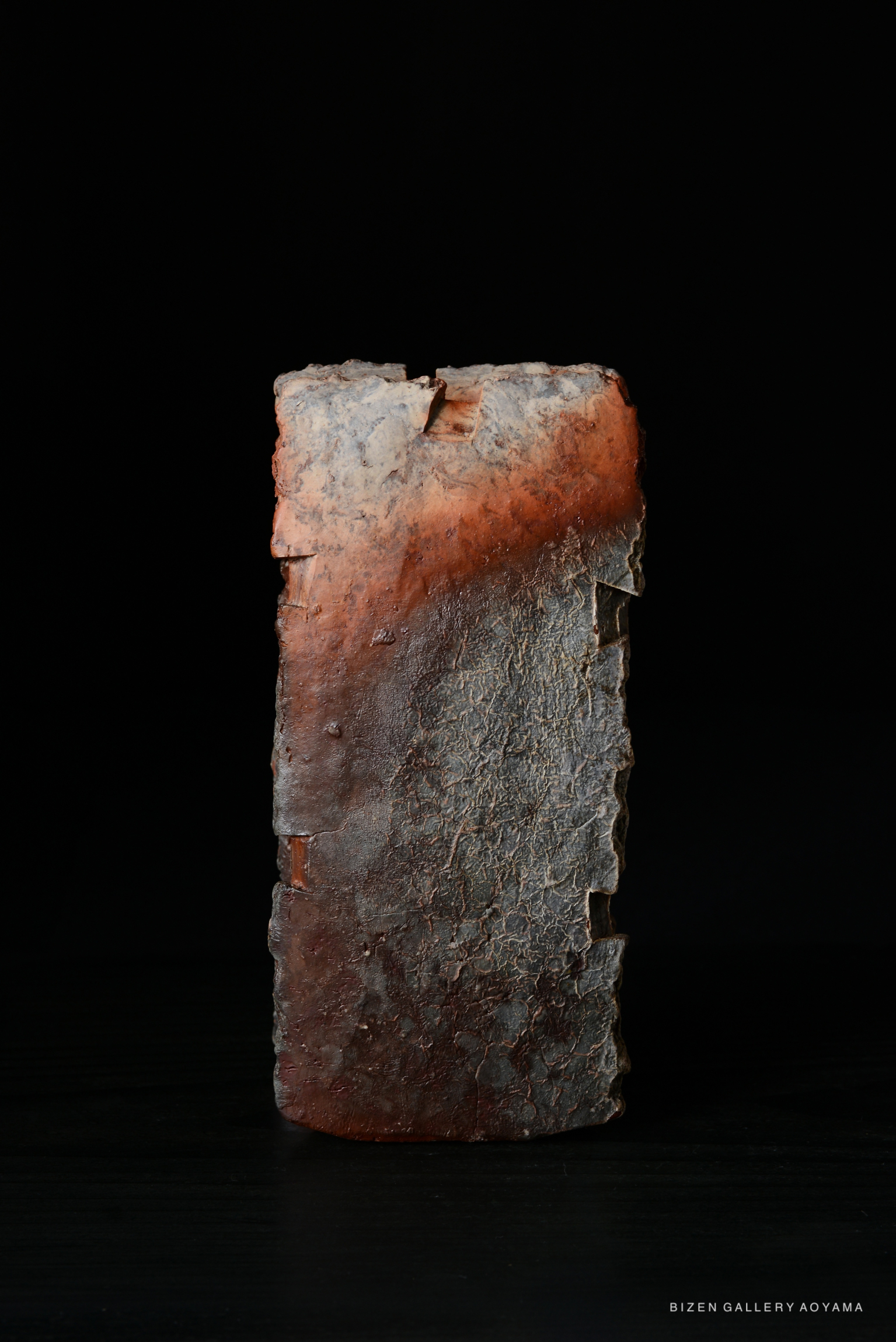 A unique piece of Bizen ware pottery featuring a textured surface and deep, original colors, displayed against a dark background.