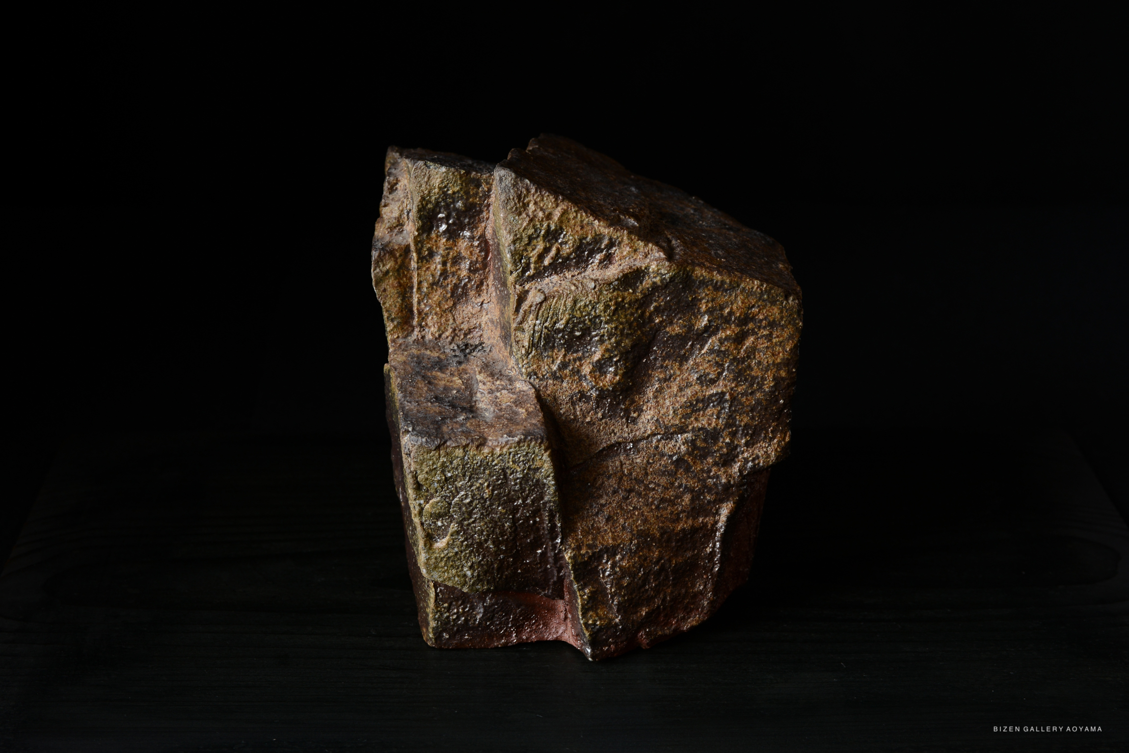 A textured rock sculpture with an irregular shape, set against a dark background.