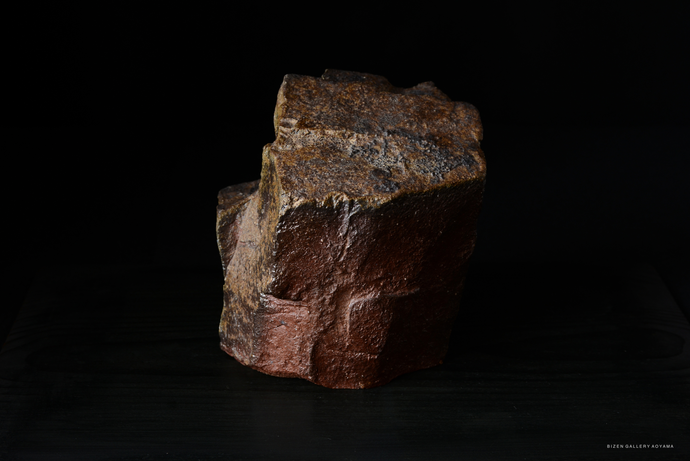 A textured, irregularly shaped pottery piece with a rich, earthy brown color, displayed against a dark background.