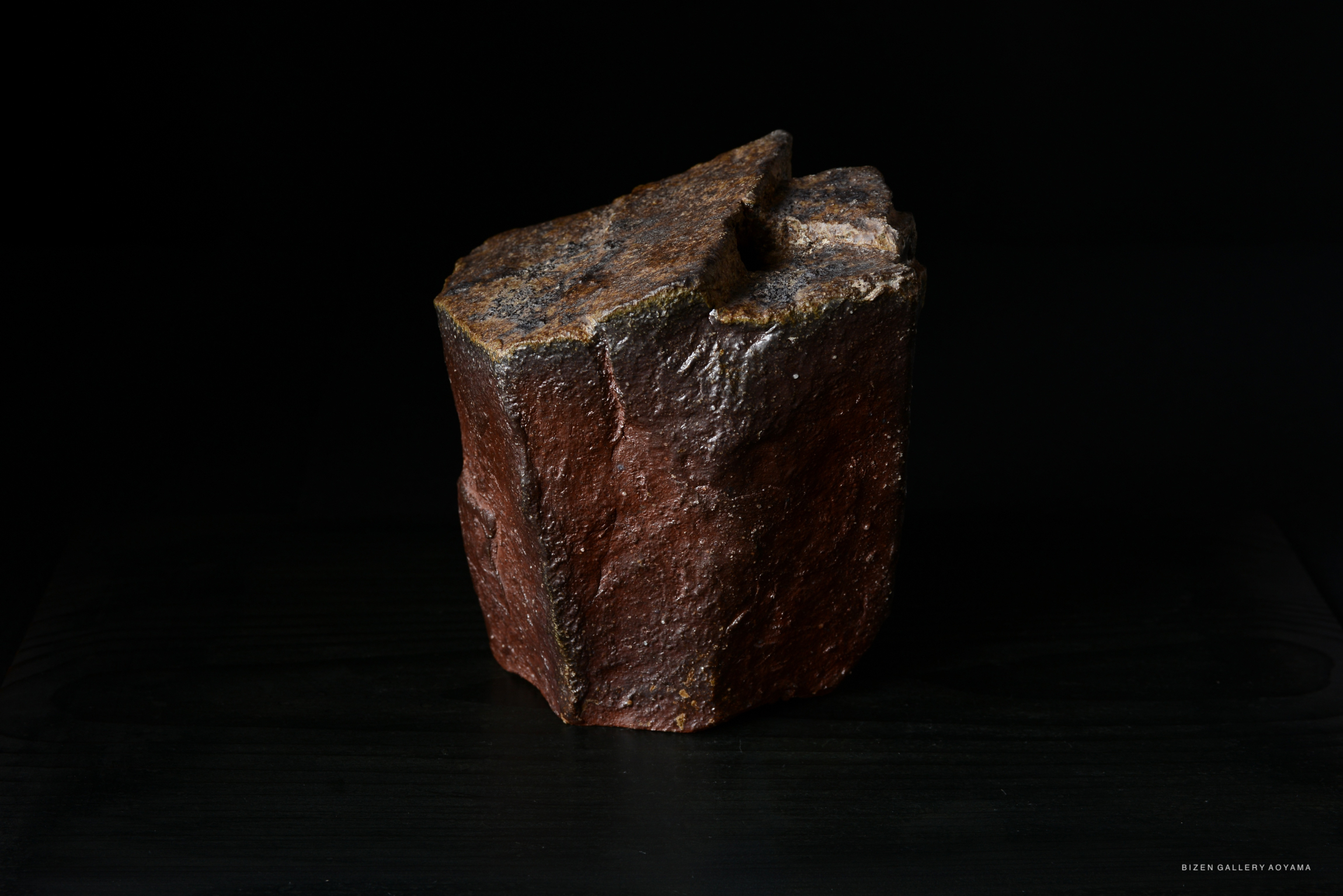 A rustic brown ceramic sculpture with a textured surface, placed on a dark background.