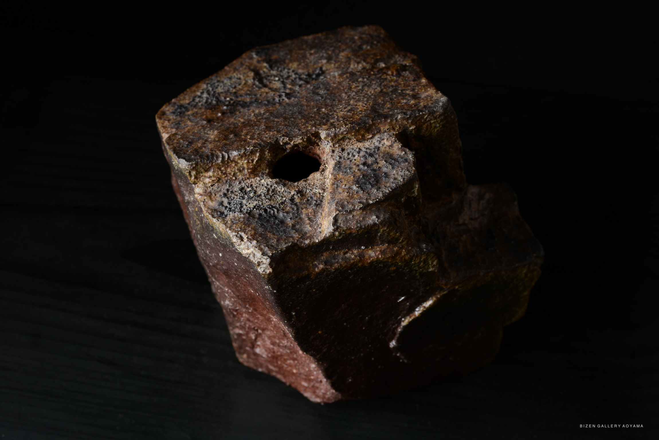 A textured rock with a rough surface and a circular hole, positioned on a dark background.