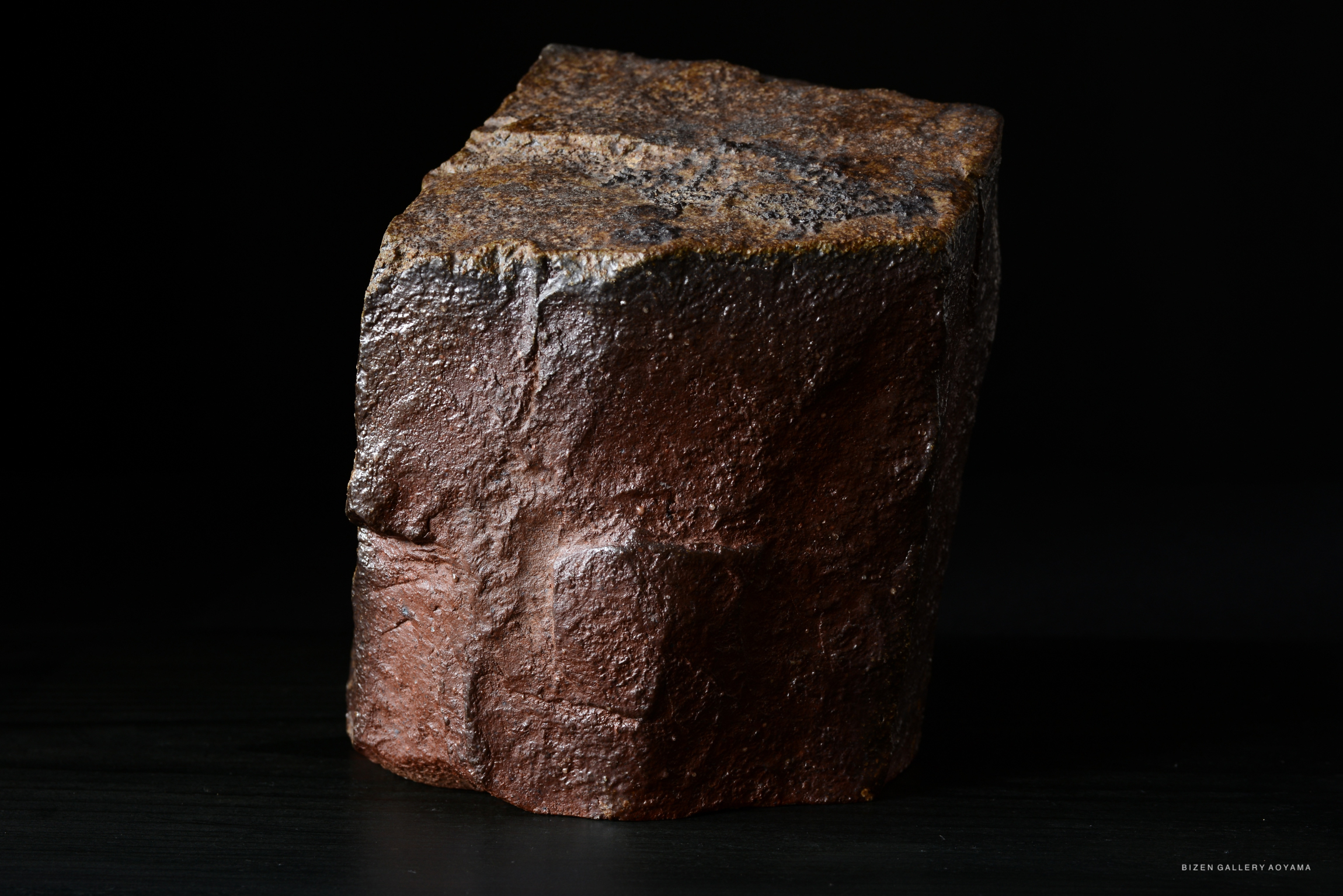 A close-up image of a textured, dark brown stone resembling a natural rock formation, set against a black background.