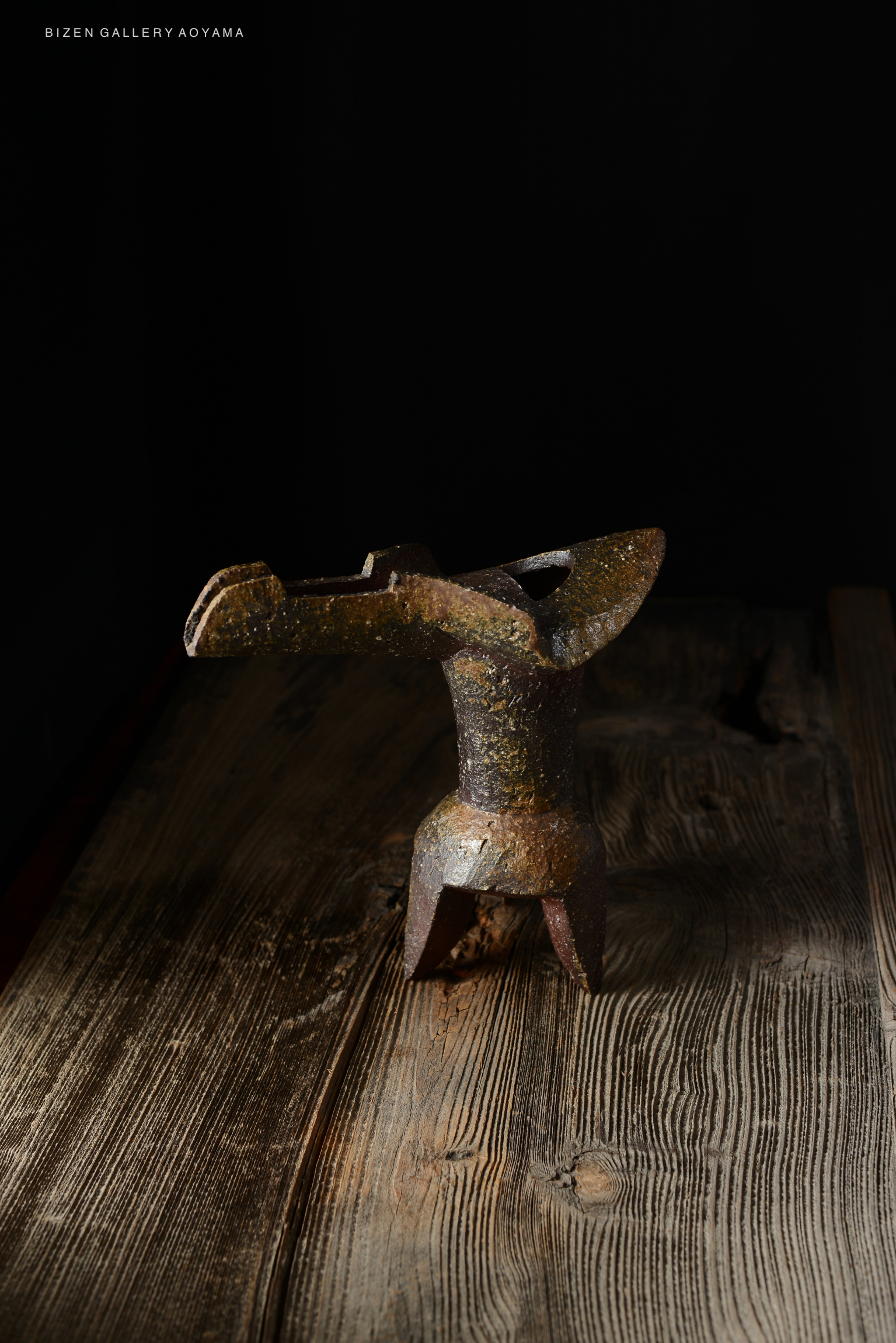 A unique, handcrafted Bizen ware sculpture with a distinct shape, resting on a wooden surface under soft lighting.