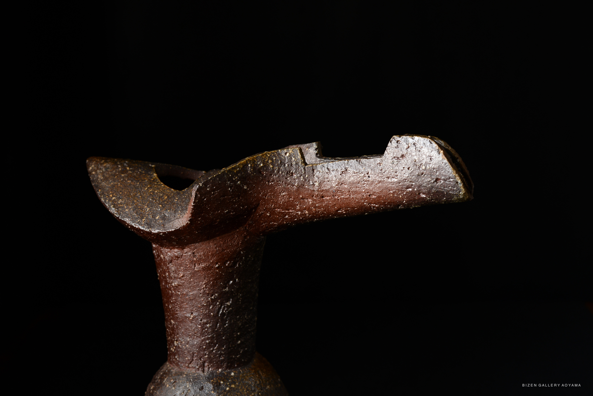 A close-up image of a unique ceramic vase with a textured brown surface, featuring a distinctive, sculptural design and a wide opening at the top.