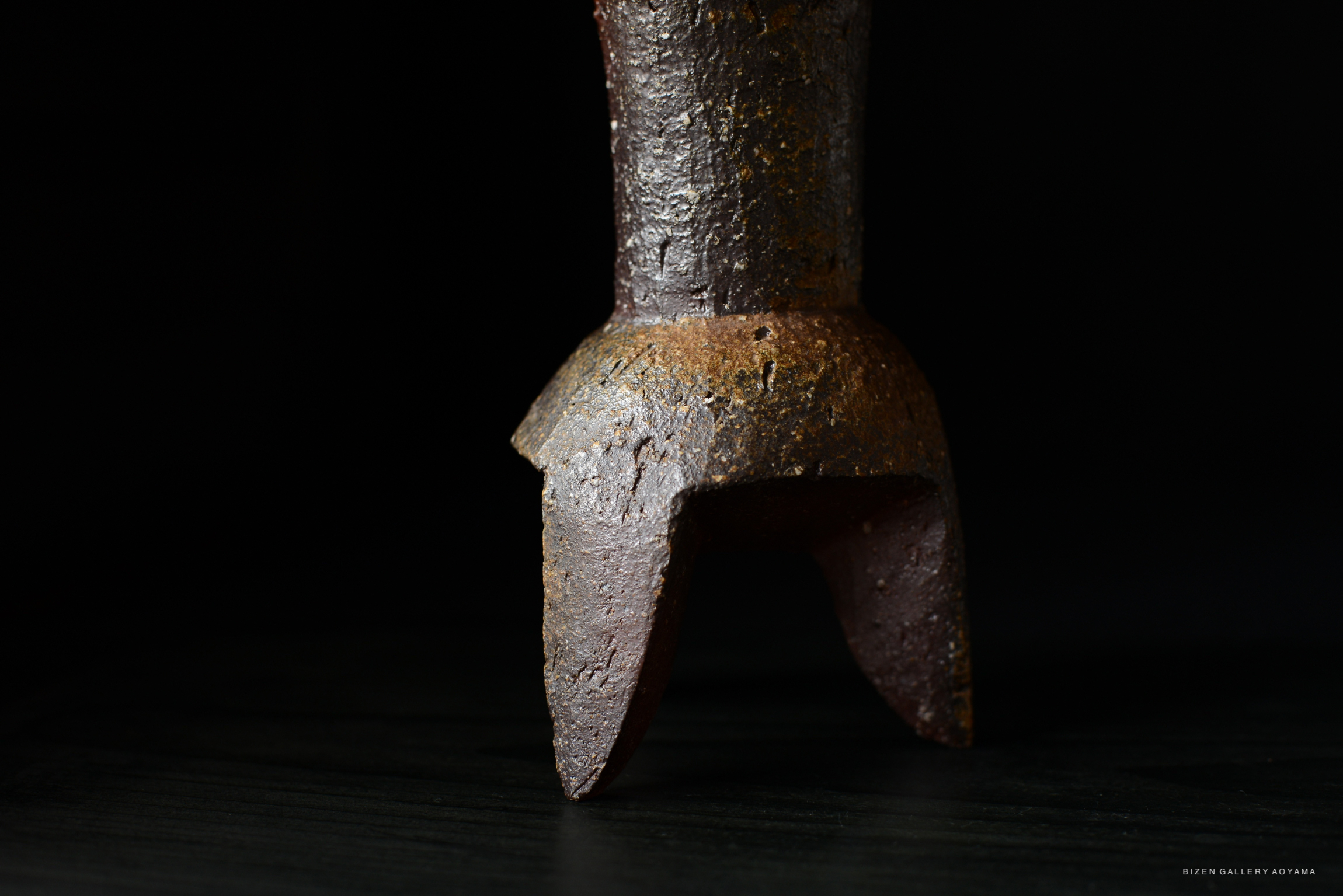 A close-up image of a ceramic vase or flower container with a textured surface, displayed against a dark background.