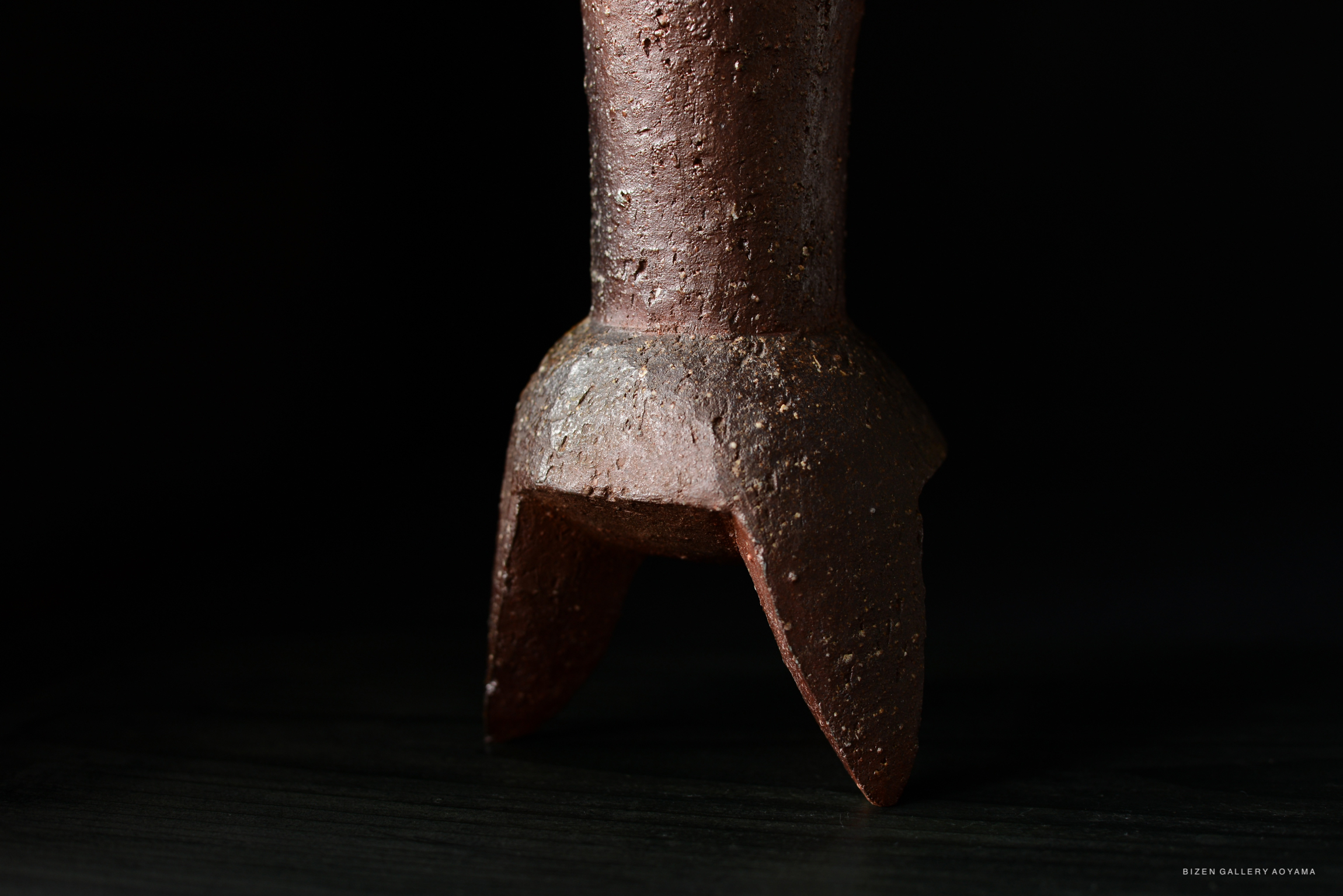 Close-up of a ceramic vase with a textured surface and a triangular base, set against a dark background.