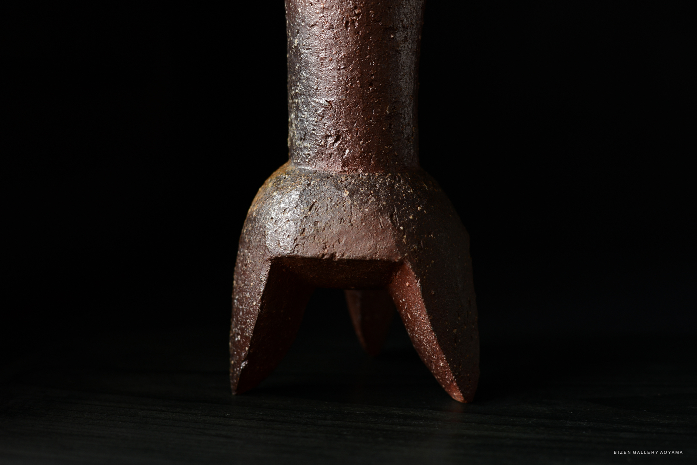 Close-up view of a ceramic vase base with a textured surface, featuring a tripod design and earthy color tones against a dark background.