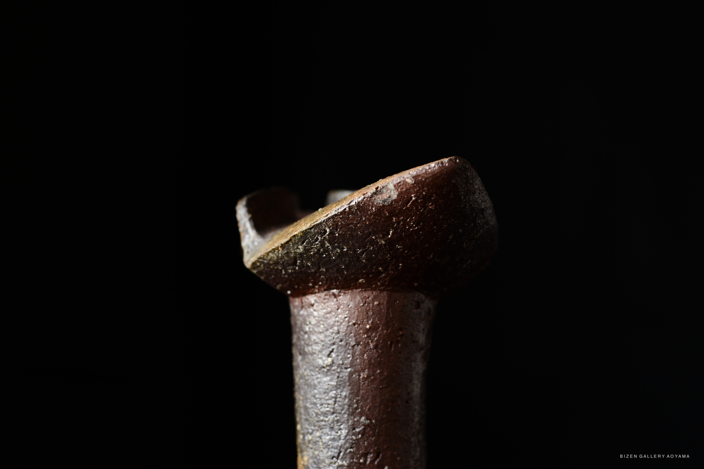 Close-up of a ceramic vase with a distinctive shape and texture, set against a dark background.