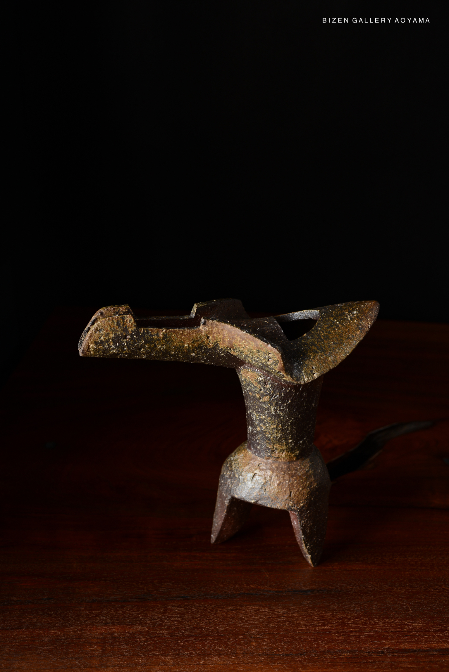 A decorative ceramic vase with a unique design, featuring a textured surface and a dark color palette, displayed on a wooden surface against a black background.
