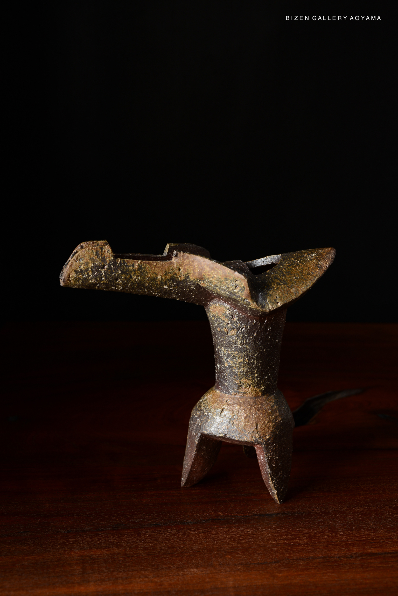 A rustic ceramic hanaire (flower vase) with an abstract design, featuring earthy tones, displayed on a wooden surface against a dark background.