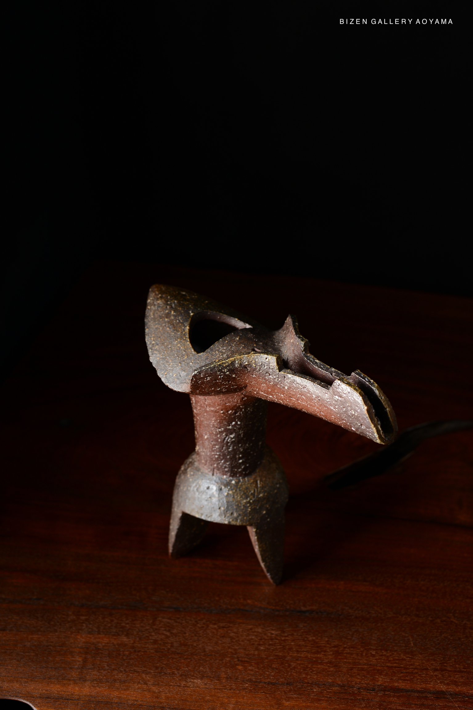 A decorative ceramic vase with a unique, artistic design, placed on a wooden surface against a dark background.