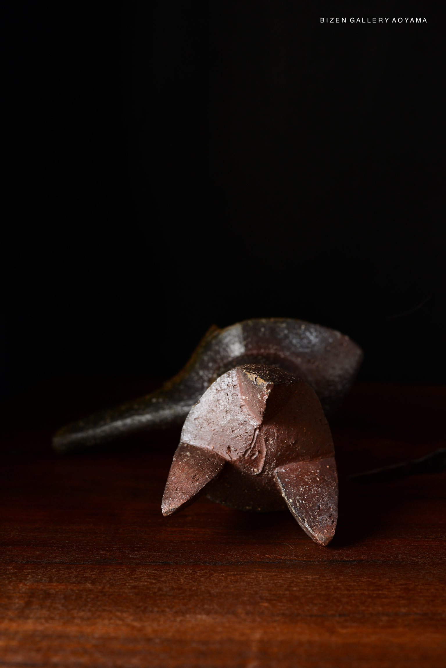 A Bizen ceramic flower vase with a unique geometric design, placed on a wooden surface against a dark background.