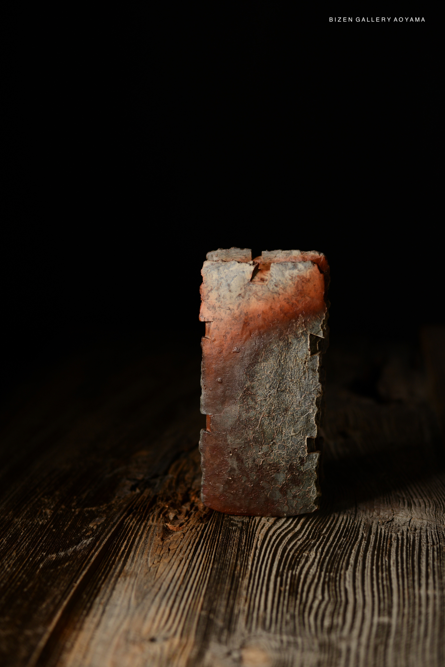 A rustic piece of pottery with a textured, reddish-brown surface, displayed against a dark background.