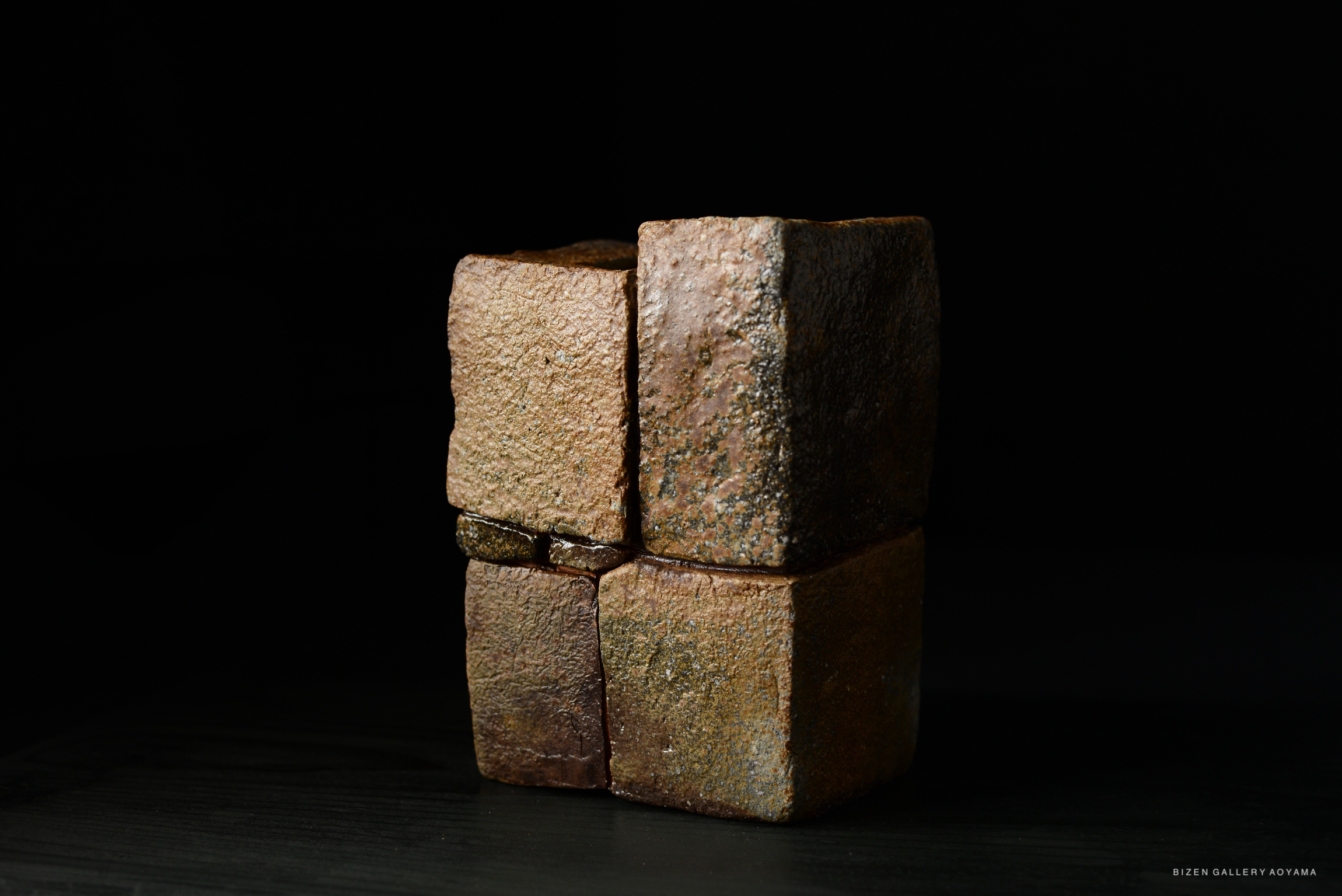 A close-up image of a unique Kumiishi Hanaire pottery piece, featuring four irregularly shaped clay blocks stacked together on a dark background.