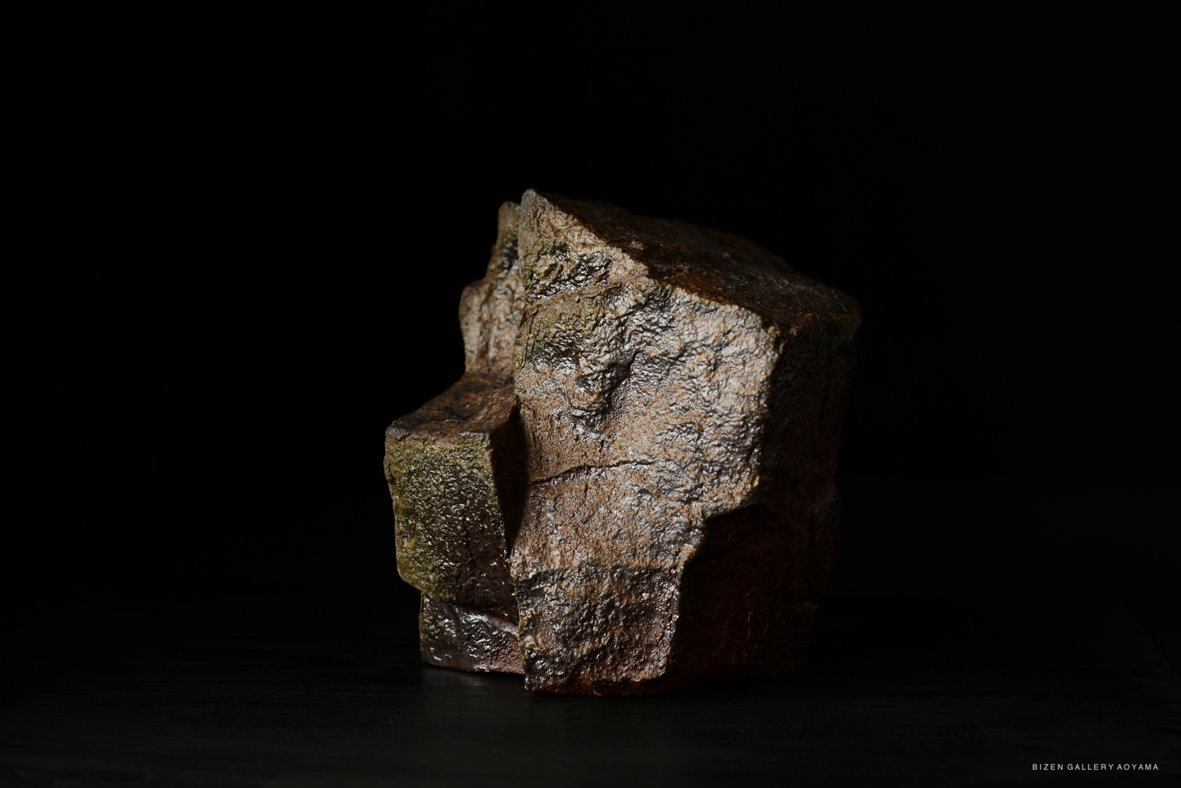 A textured brown rock sculpture with a rugged surface, set against a black background.