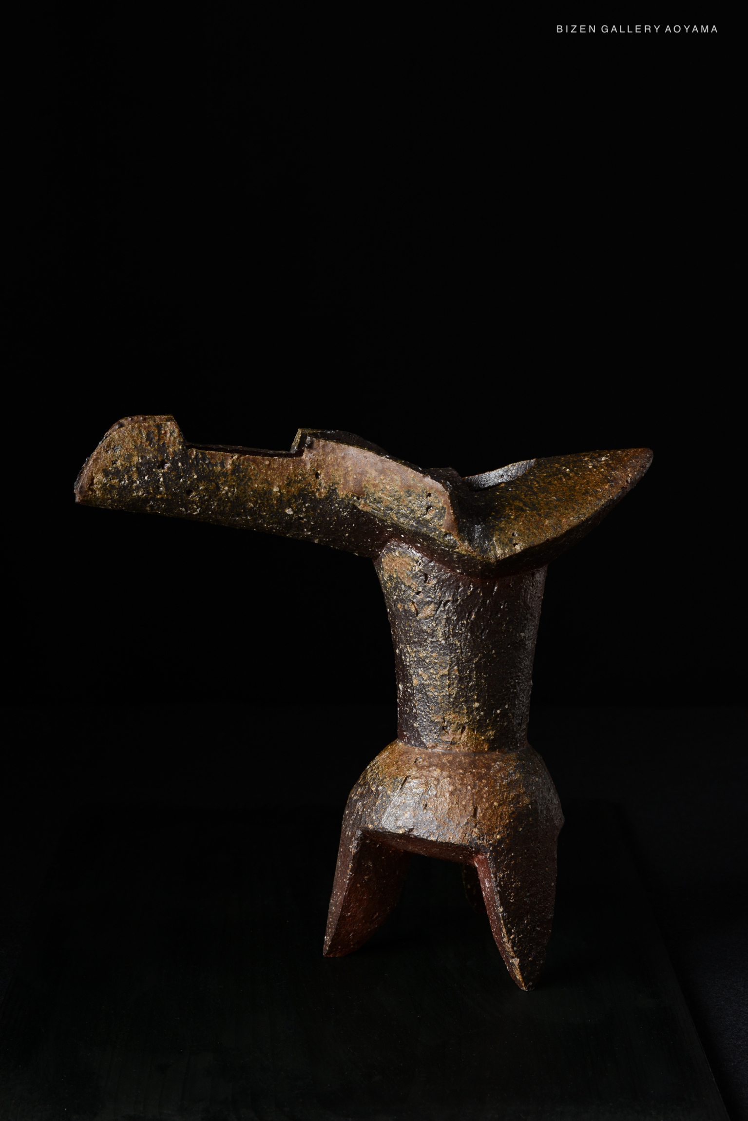 A sculptural ceramic vase with an abstract design, featuring a textured surface and dark coloration, displayed against a black background.