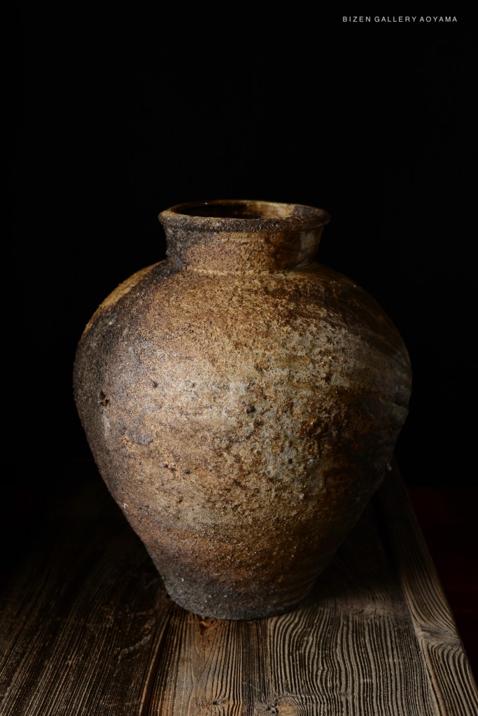 A close-up of a traditional Bizen pottery vase, displaying its textured surface and earthy colors against a dark background.
