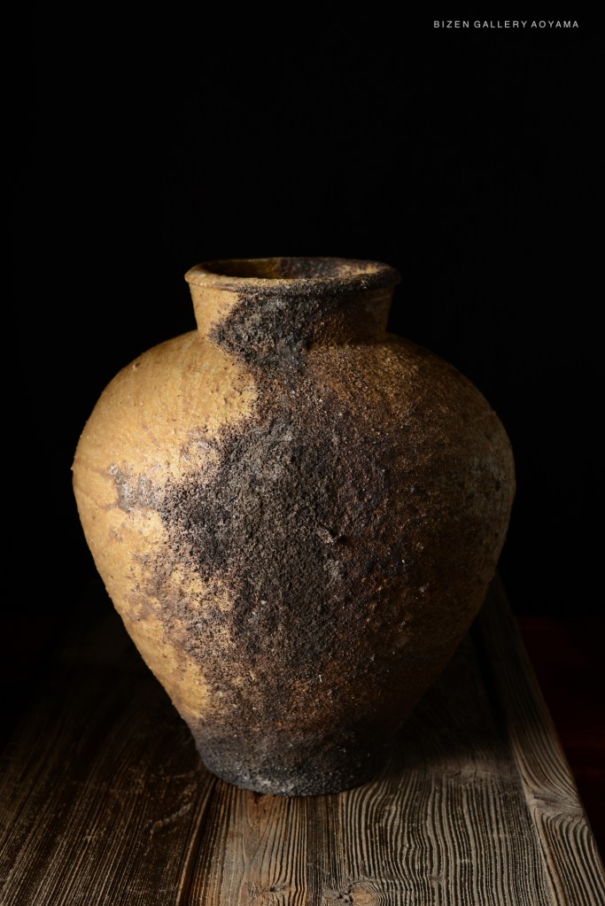 A Bizen pottery vase with a textured surface and earthy tones, presented on a wooden surface against a black background.
