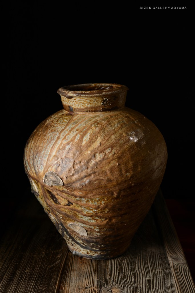 A Bizen pottery jar with a textured brown surface and subtle variations in color, displayed against a dark background.