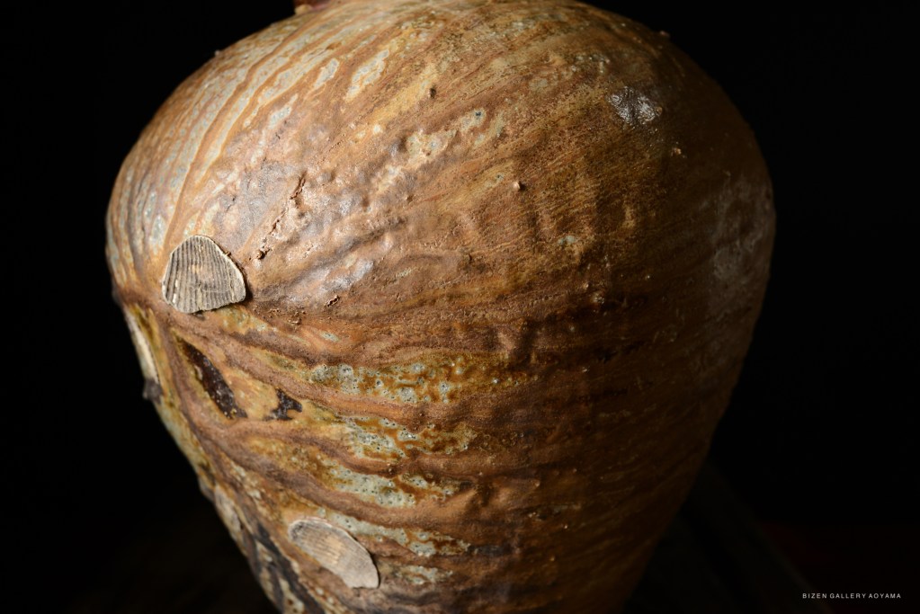 Close-up of a Bizen pottery tsubo, showcasing its textured surface and natural imperfections against a black background.