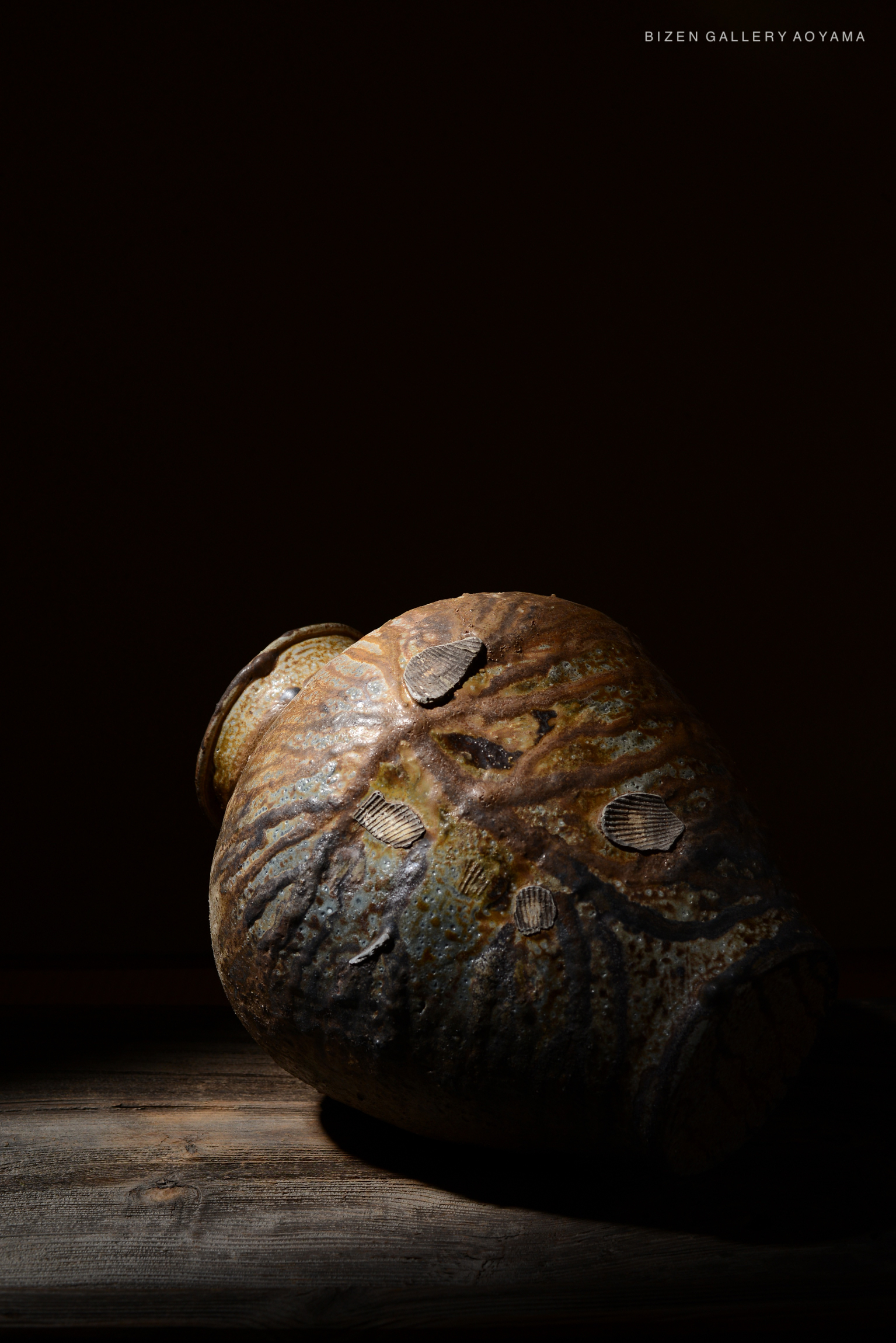 A Bizen pottery vase with a textured surface and unique markings, illuminated against a dark background.