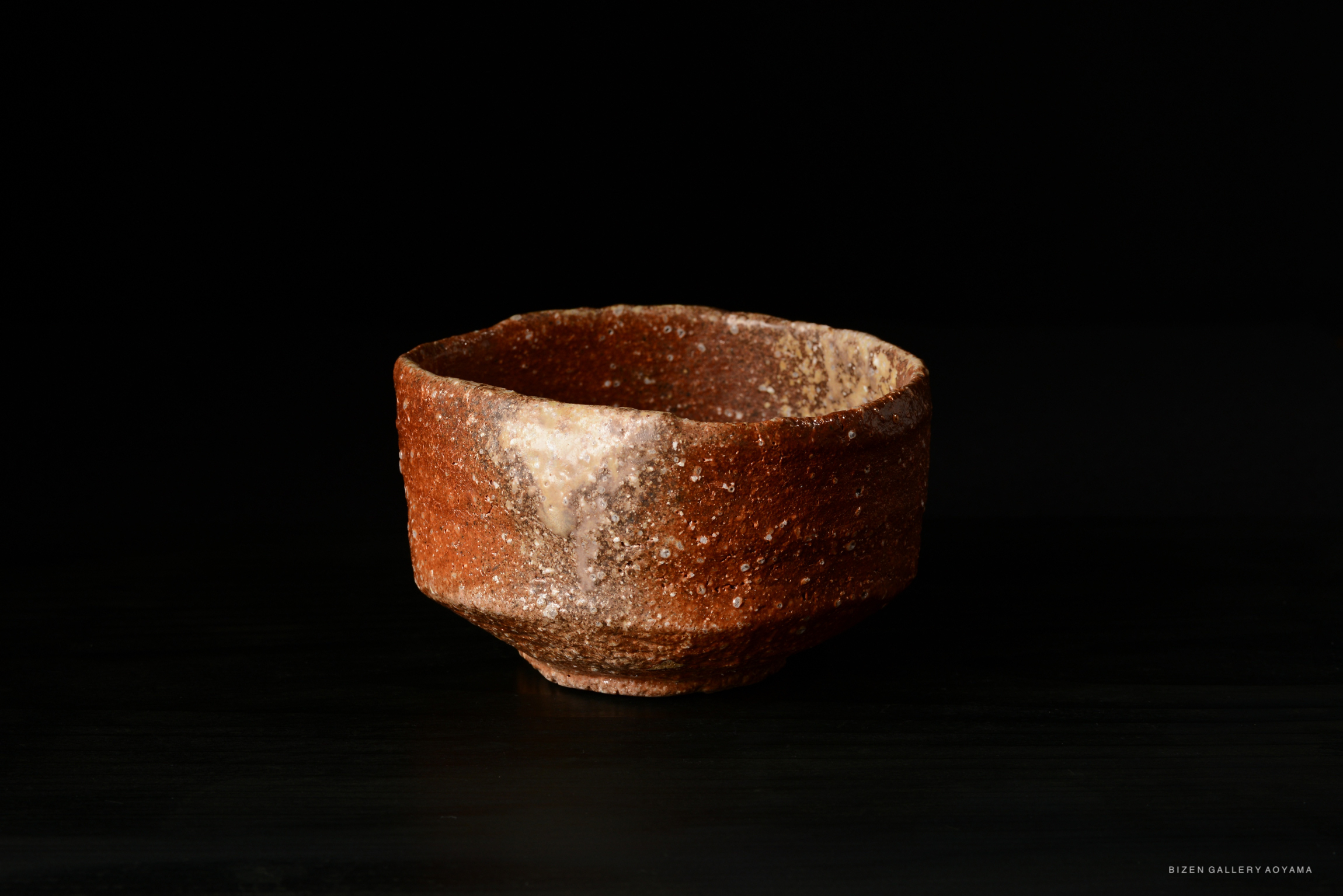 A rustic ceramic bowl with a textured surface, predominantly brown with lighter speckles, set against a dark background.