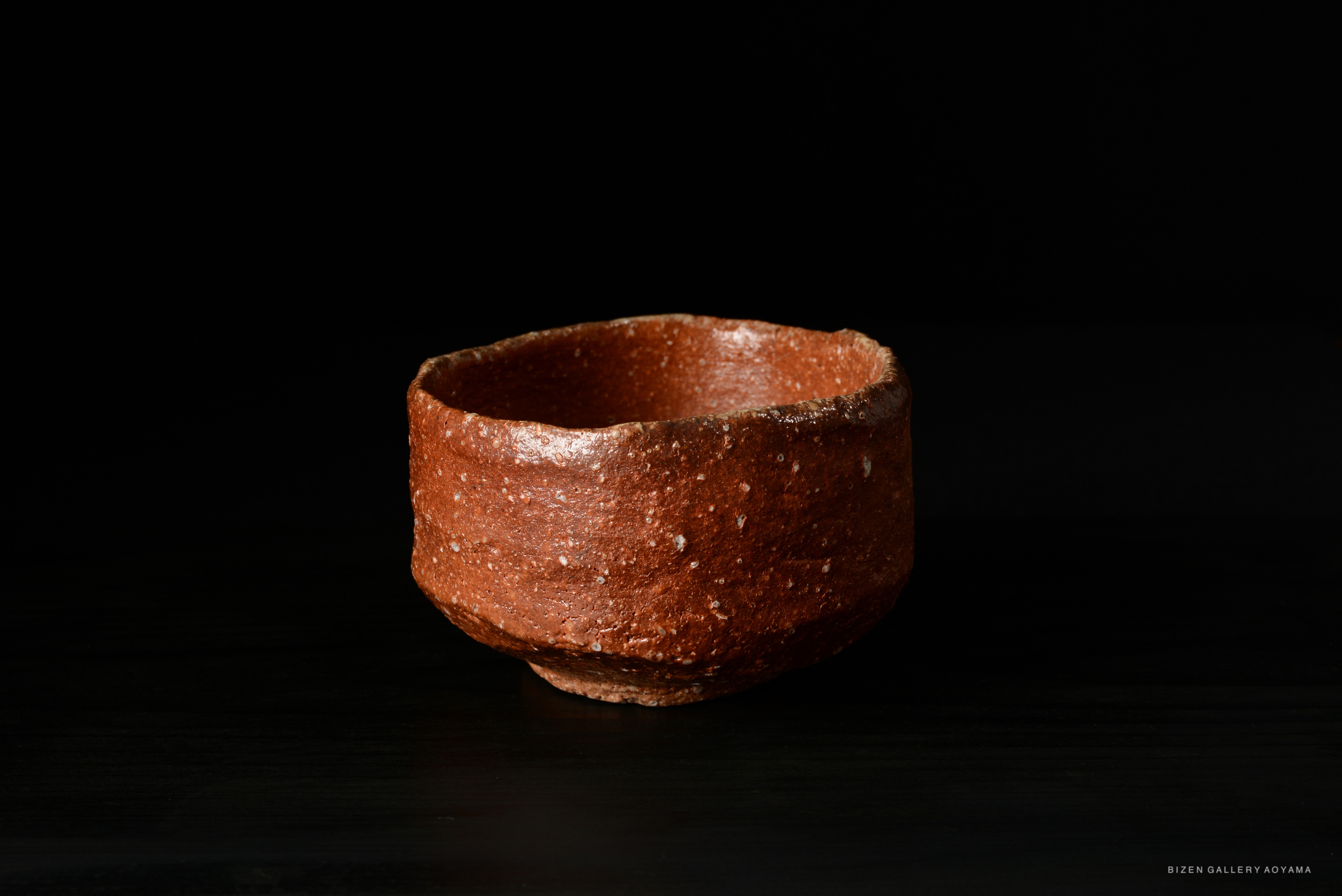 A brown ceramic cup with a textured surface, set against a black background.
