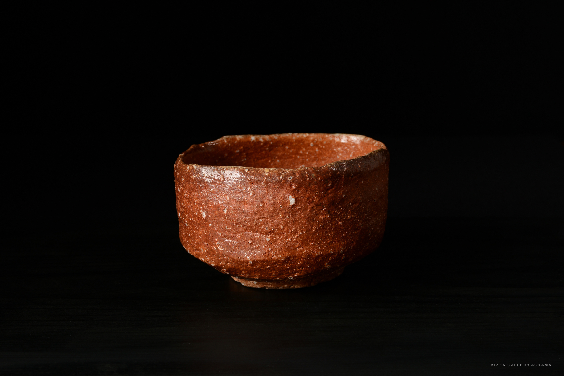 A small, rustic brown ceramic bowl placed on a dark surface, with a textured and uneven rim.