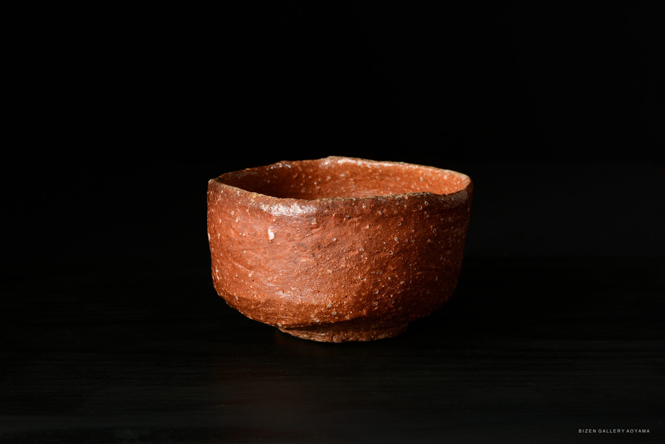 A handcrafted brown ceramic bowl with a rough texture, set against a dark background.