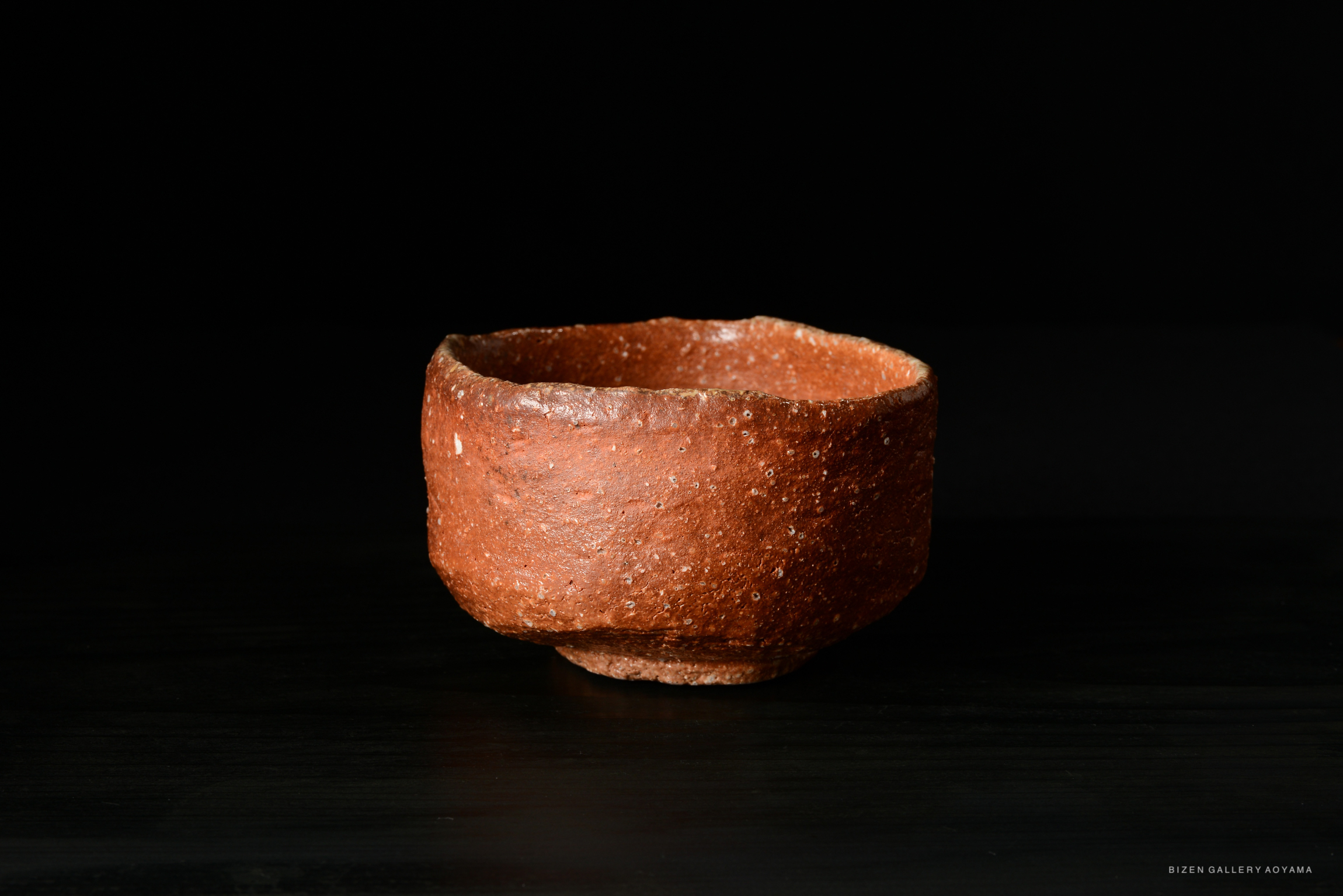 A rustic, brown ceramic bowl with a textured surface, displayed against a black background.