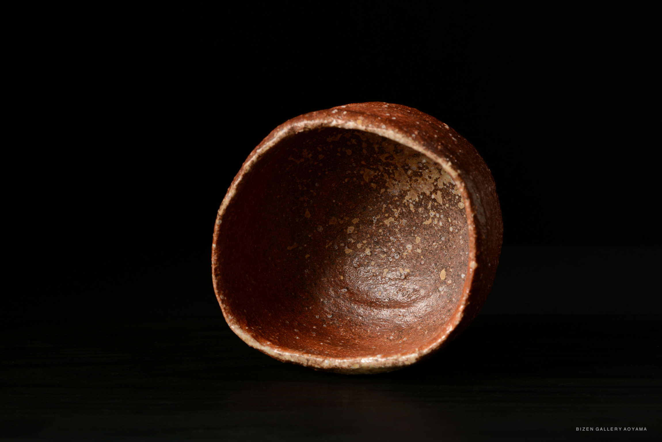 A close-up image of a traditional Bizen pottery bowl, showcasing its textured surface and earthy colors against a dark background.