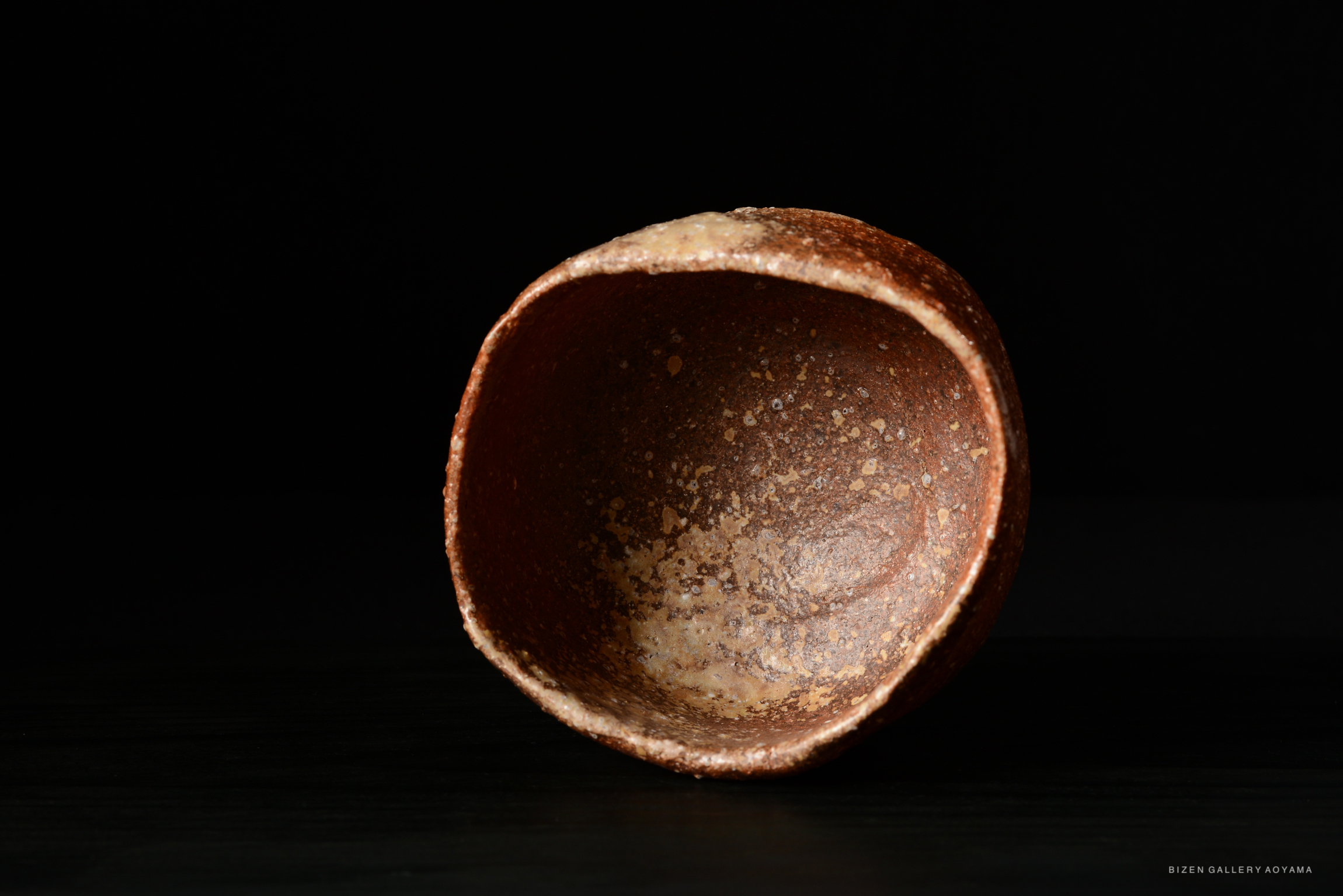 A close-up view of a brown pottery bowl with a textured surface, set against a black background.