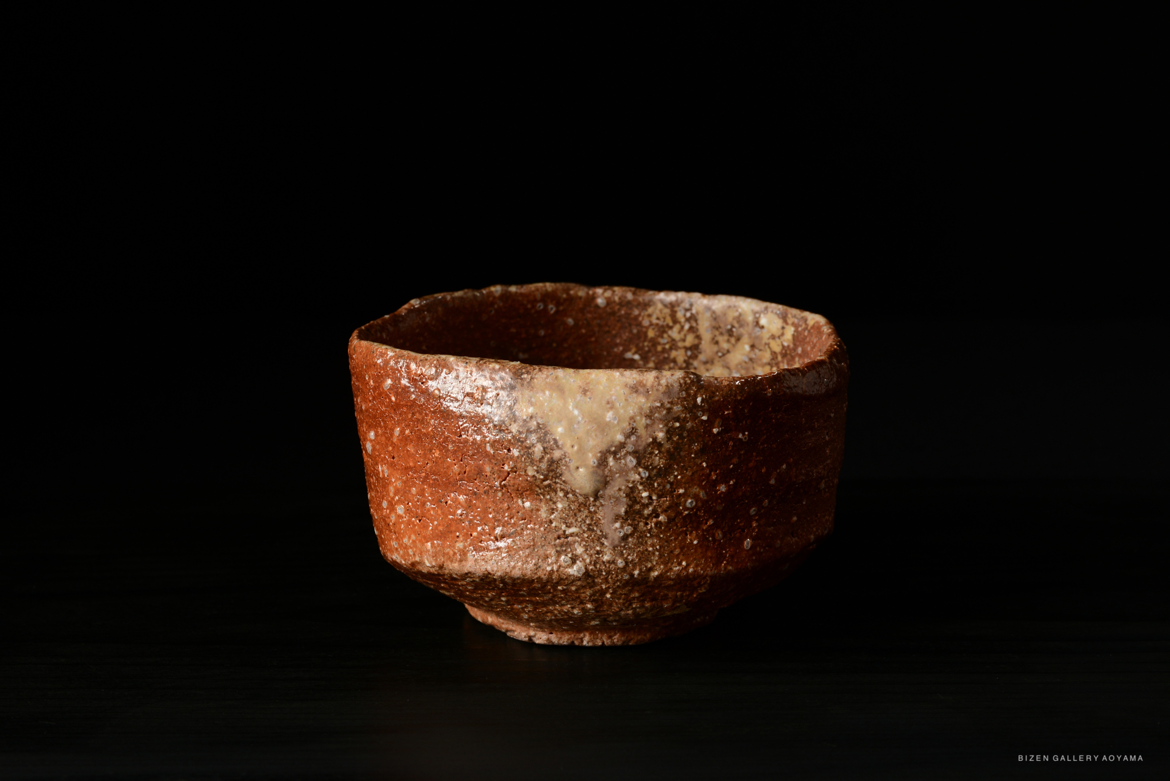 A artistic brown ceramic bowl with a textured surface, set against a dark background.