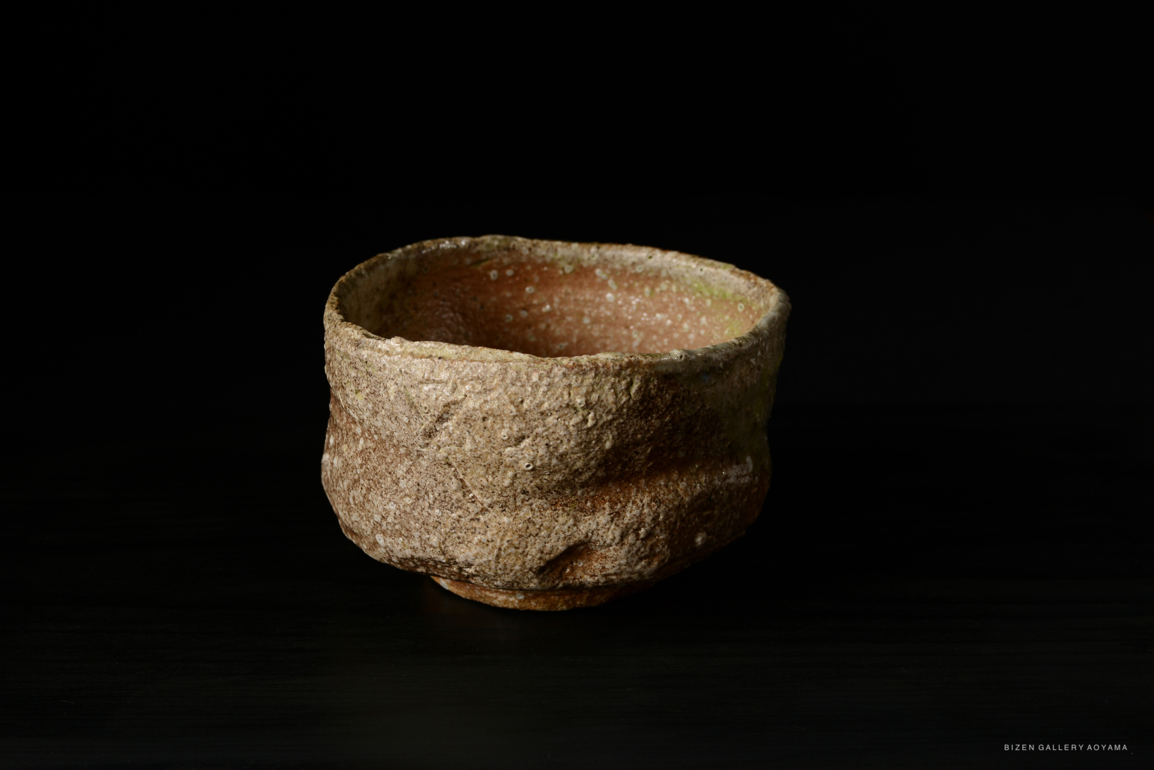 A rustic, handmade Shigaraki tea bowl with a textured, earthy exterior, displayed against a dark background.