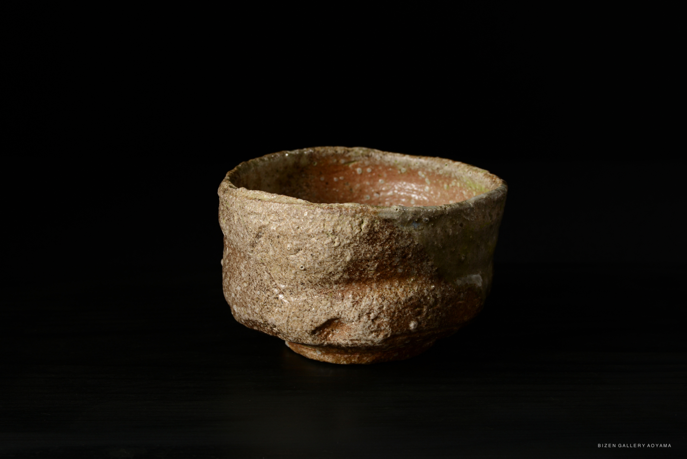 A rustic and textured Shigaraki tea bowl with a natural finish, showcasing earthy tones and an organic shape, set against a dark background.