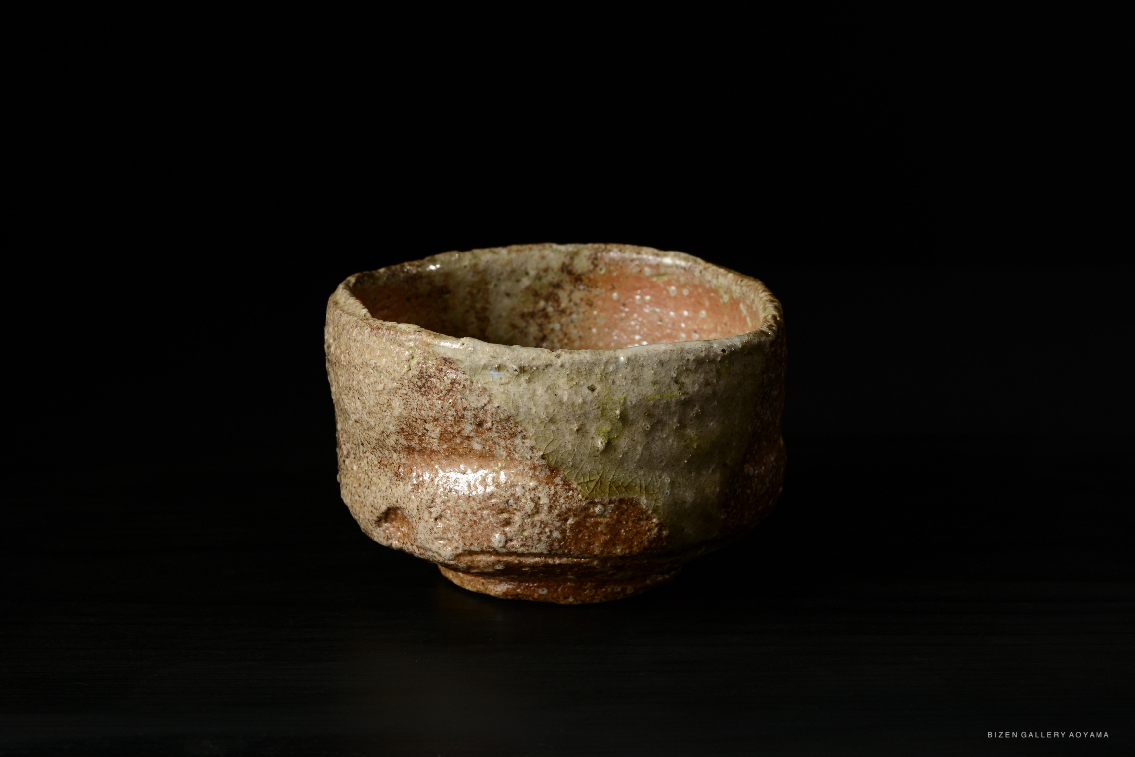 A textured, rustic tea bowl made of Shigaraki clay, featuring organic shapes and earthy tones against a dark background.