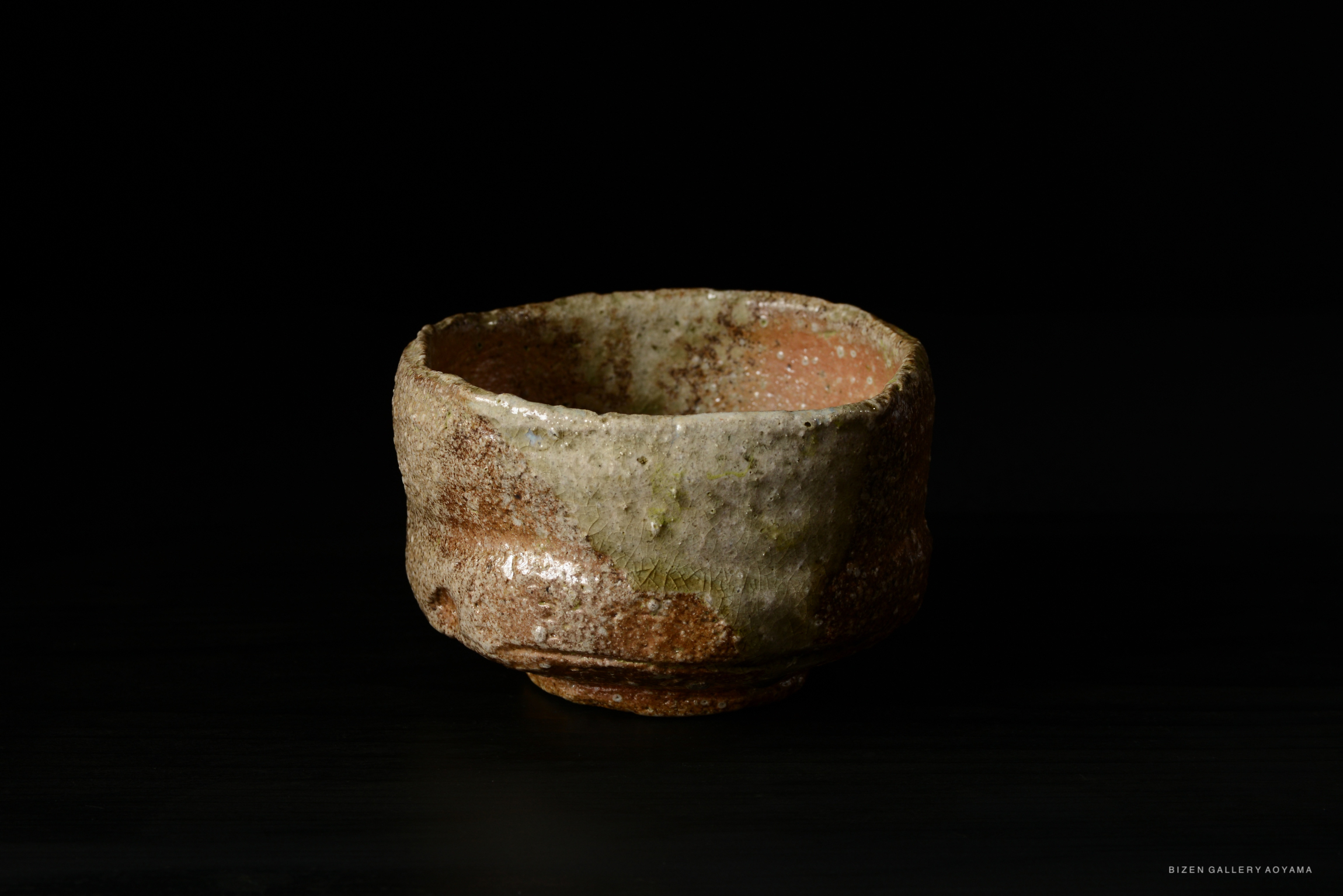 A rustic Shigaraki tea bowl with a textured surface, showcasing earthy tones and a handmade aesthetic, set against a black background.
