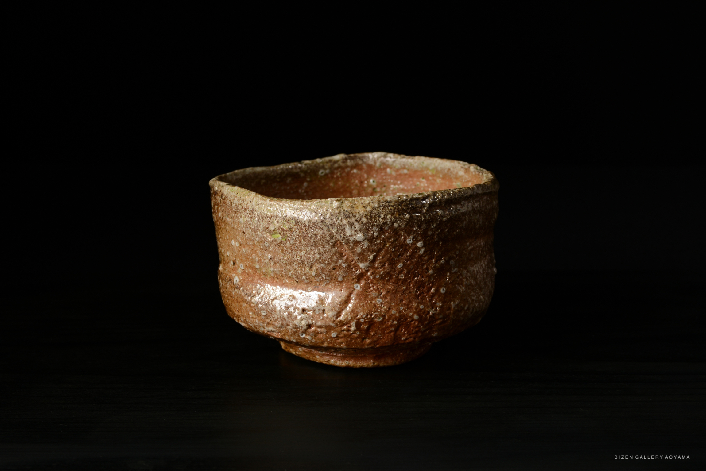 A rustic Shigaraki tea bowl with a textured surface and natural earthy tones, displayed against a dark background.
