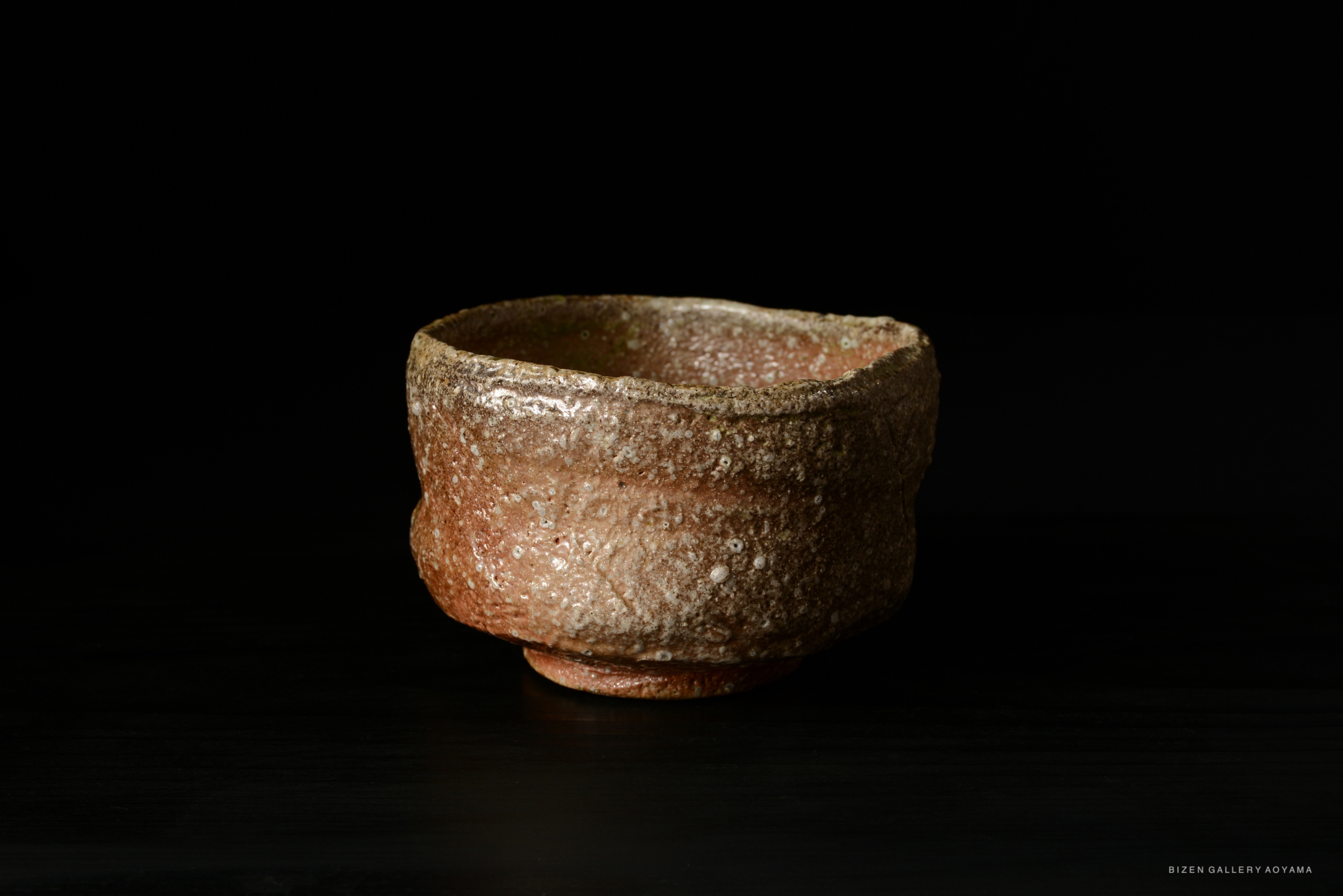 A rustic and textured Shigaraki tea bowl with earthy tones, set against a dark background.