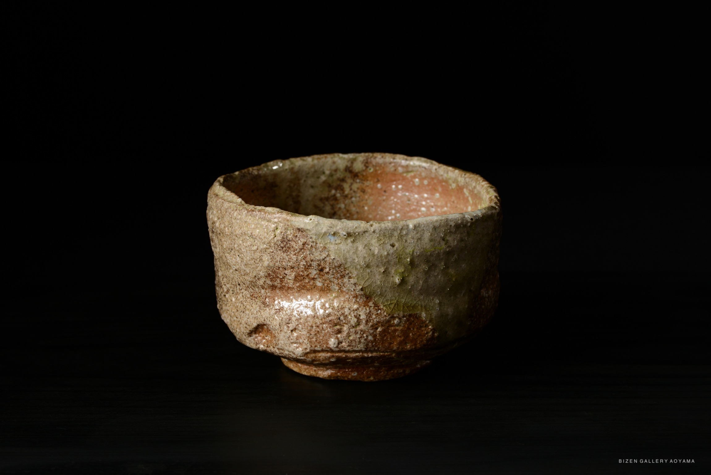 A rustic Shigaraki tea bowl with a textured surface and natural earthy colors, set against a black background.