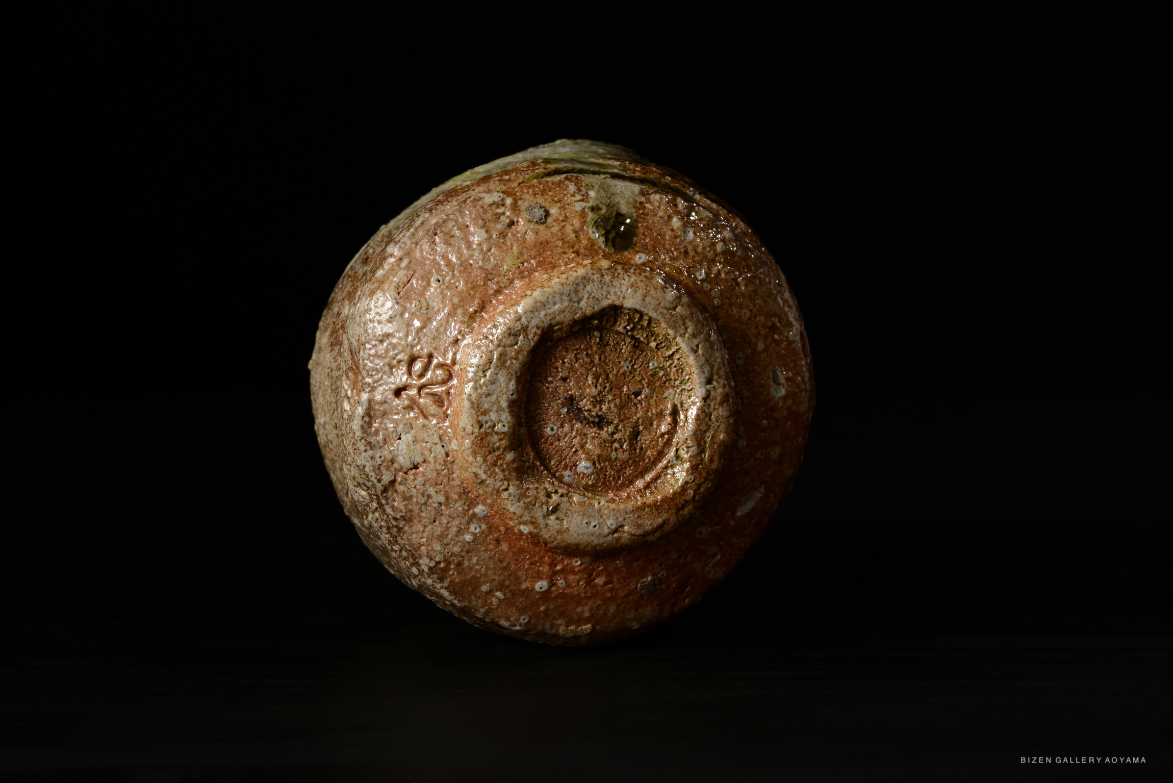 Close-up view of the底 of a rustic Shigaraki tea bowl, showcasing its textured surface and earthy colors against a dark background.