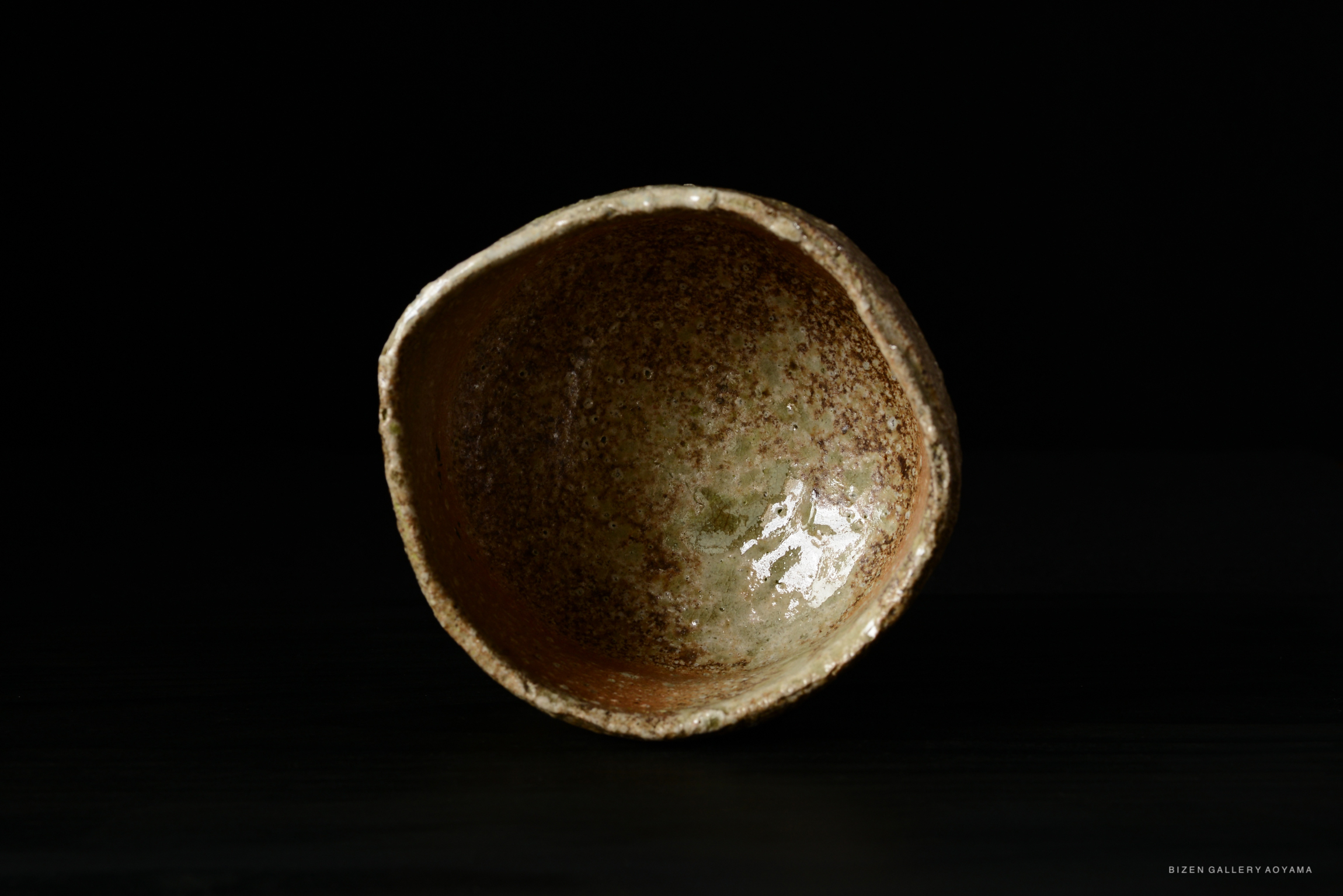 An interior view of a rustic ceramic tea bowl with an earthy glaze, showcasing textured surfaces and a muted color palette.