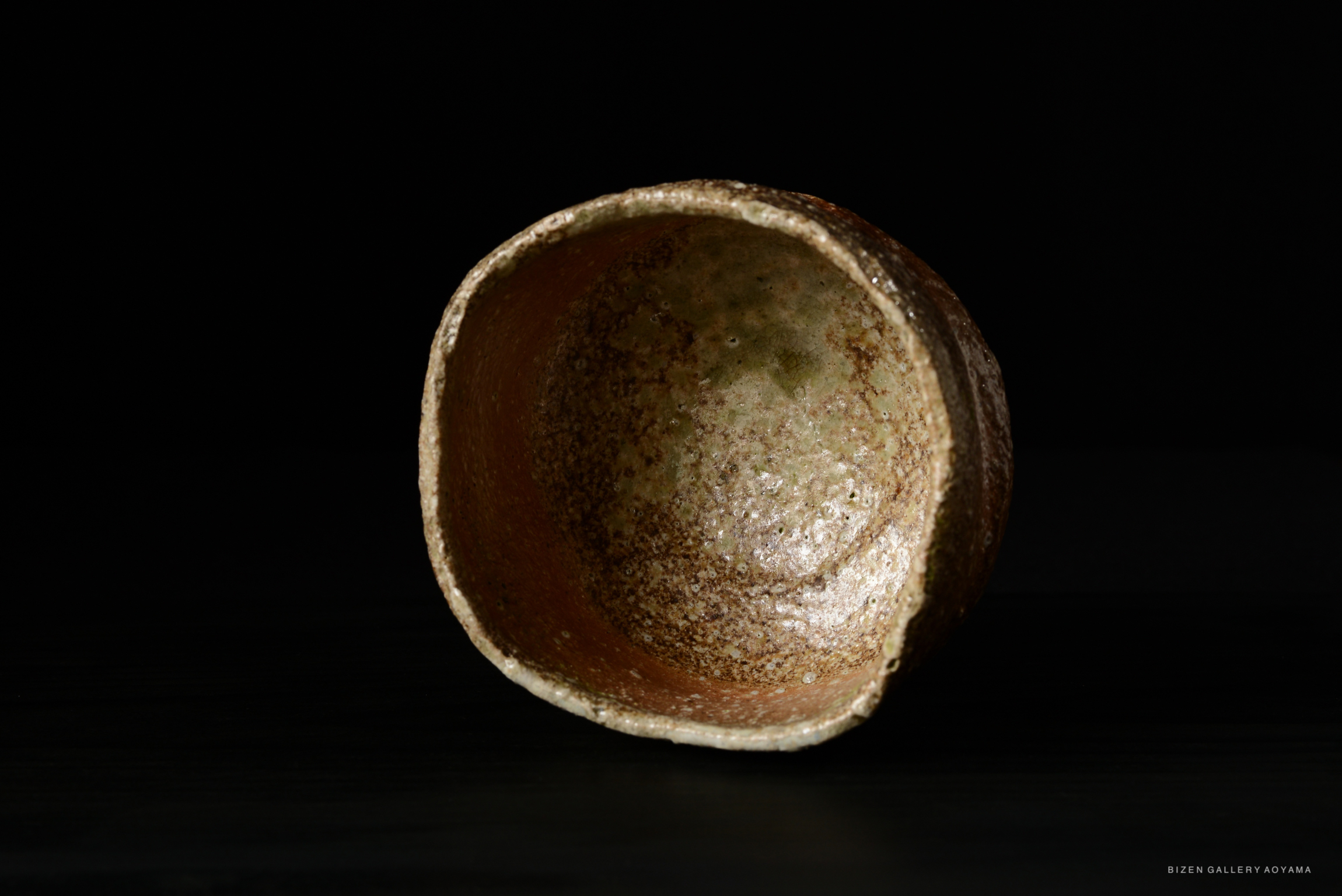 An artistic view of a rustic ceramic bowl with an earthy texture, showcasing a blend of muted greens and browns against a dark background.
