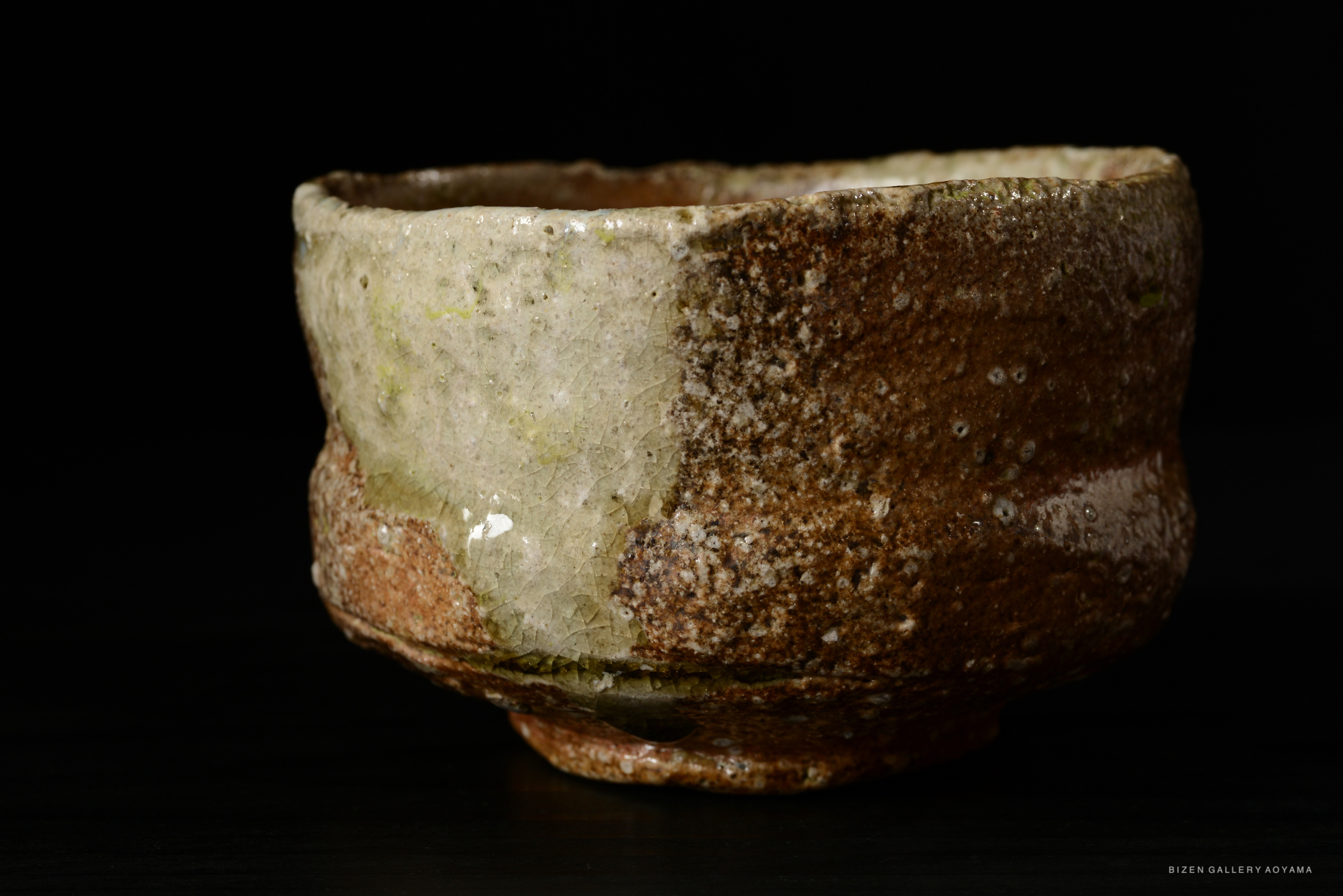 A rustic Shigaraki tea bowl with a textured surface, showcasing earthy tones and natural imperfections, displayed against a dark background.