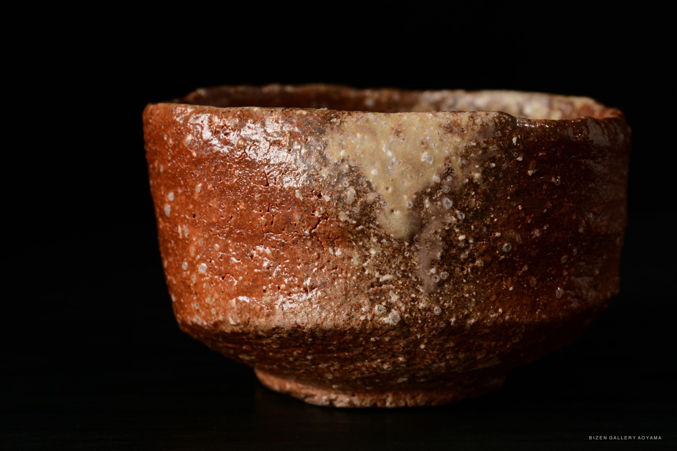 Close-up of a rustic ceramic bowl with a textured brown surface and a light-colored rim, set against a dark background.