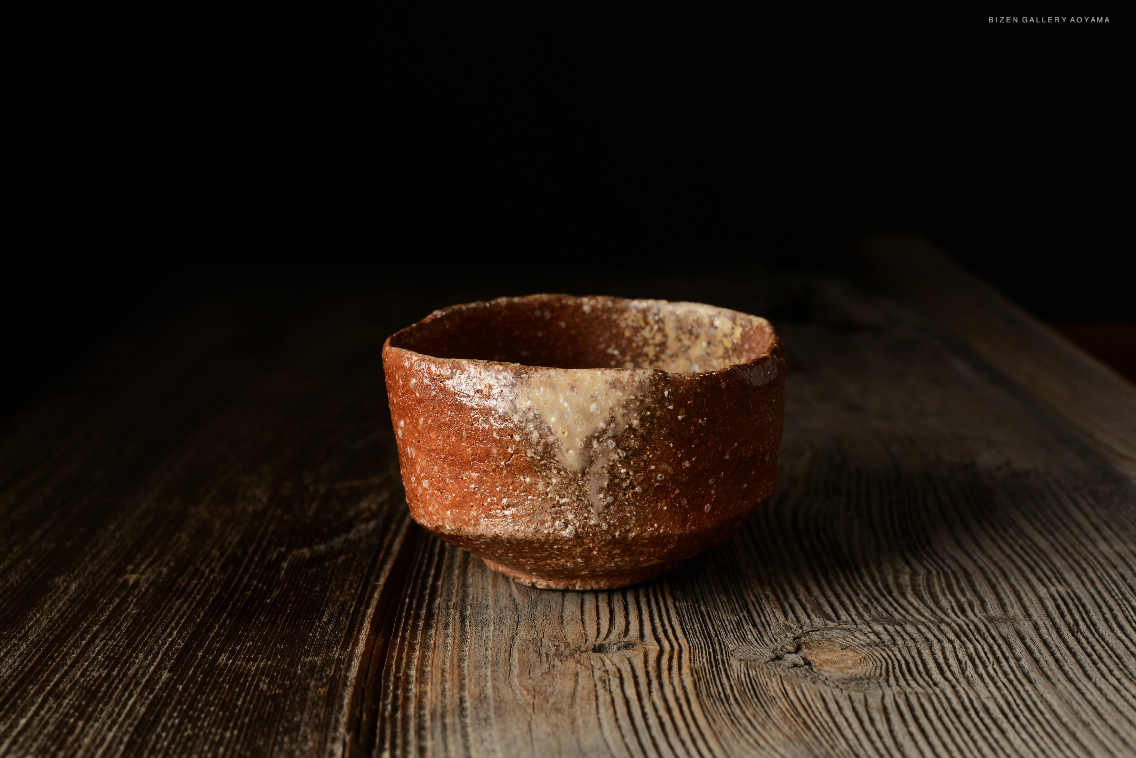 A rustic brown ceramic bowl displayed on a wooden surface with a dark background.