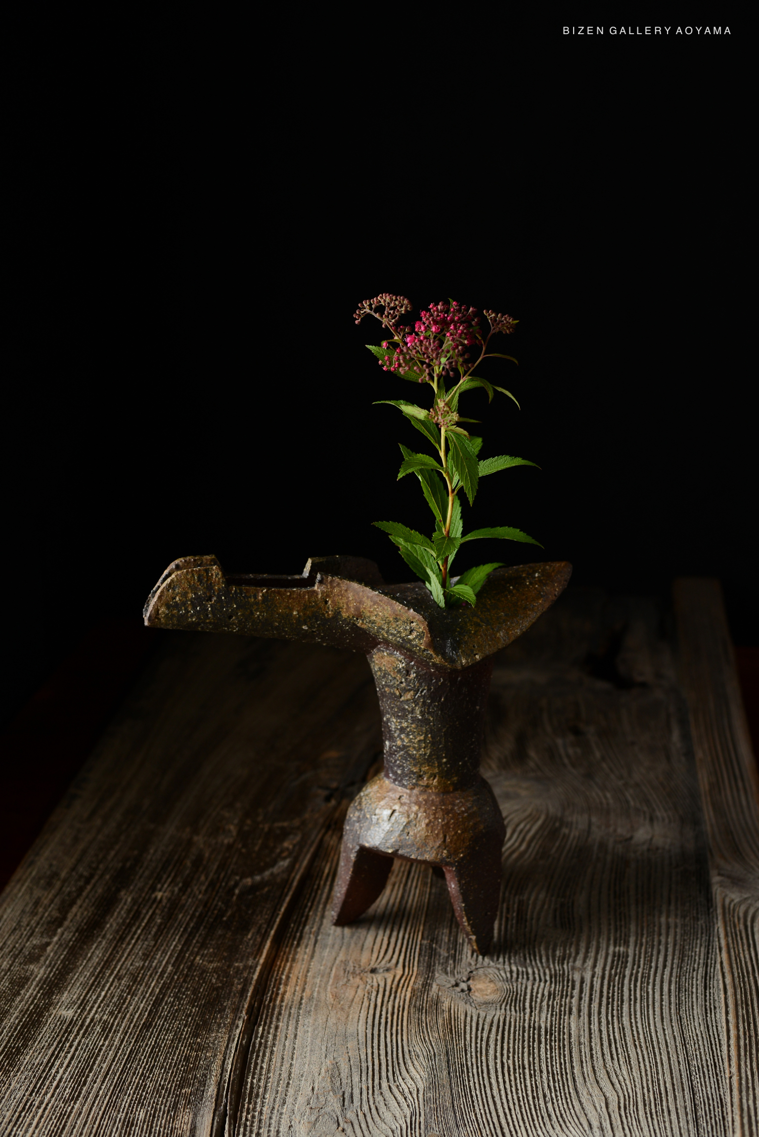 A traditional Japanese flower vase made of metal, displaying delicate flowers on a wooden table with a dark background.
